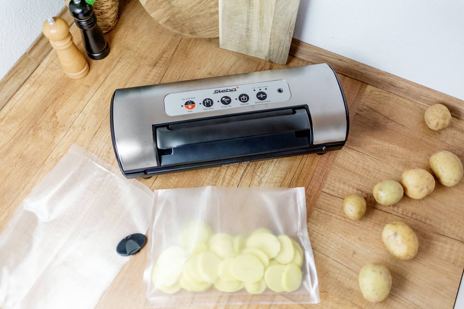 Appareil de mise sous vide sur le comptoir de cuisine, entouré de pommes de terre. Un sachet ouvert révèle des tranches de pommes de terre découpées.