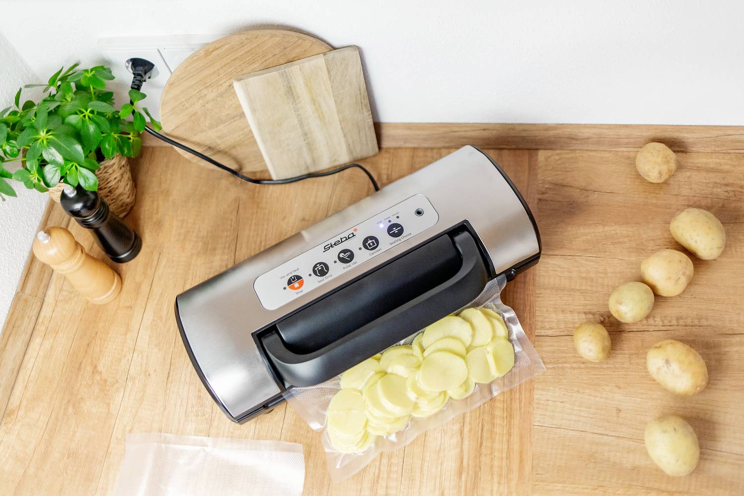 Appareil de mise sous vide posé sur une table en bois avec un sachet ouvert rempli de tranches de pommes de terre. Pommes de terre et épices sur le côté.