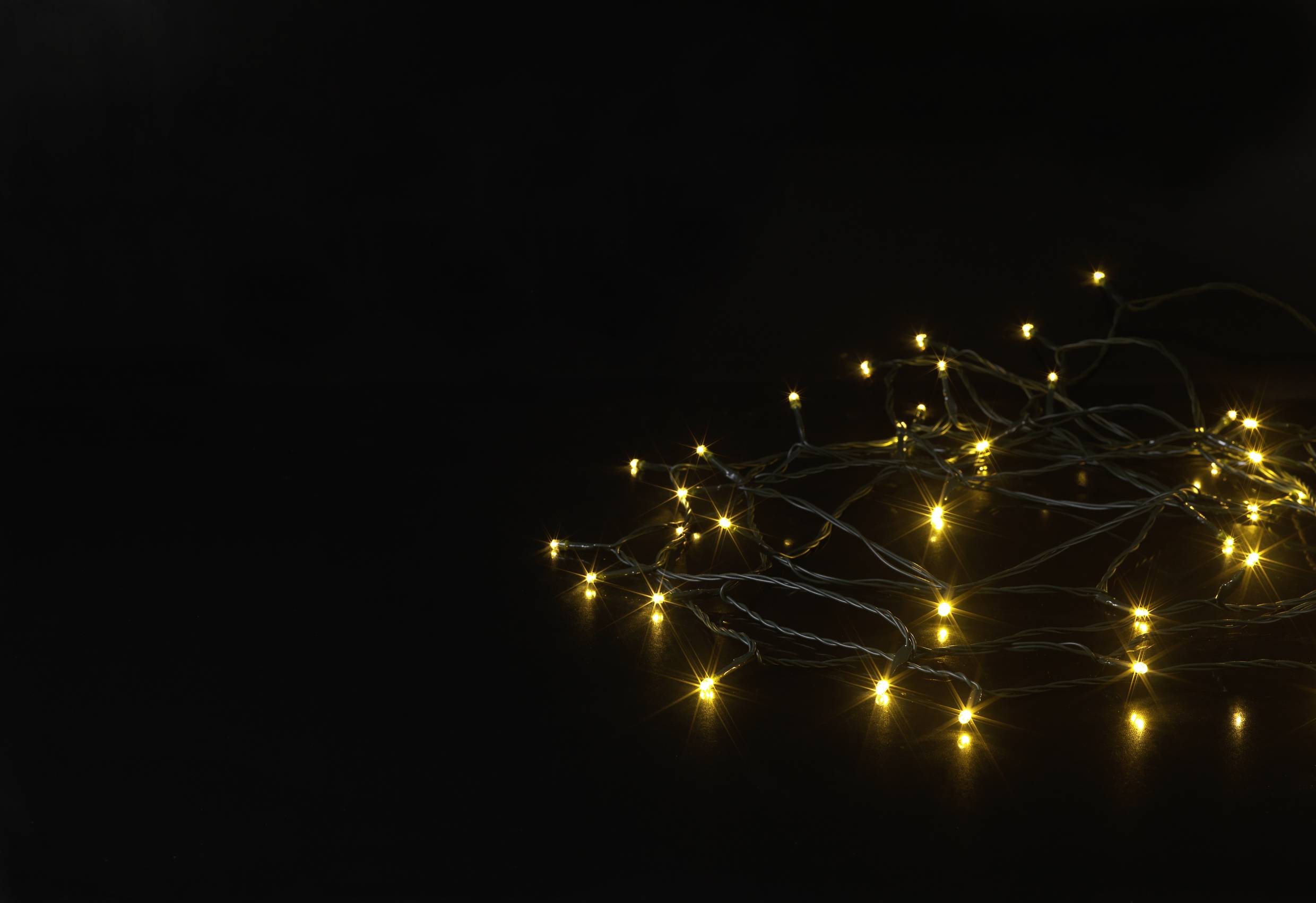 Guirlande lumineuse avec de petites lumières jaunes sur un fond sombre. Les lumières forment un motif lâche qui crée une atmosphère chaleureuse et intime.