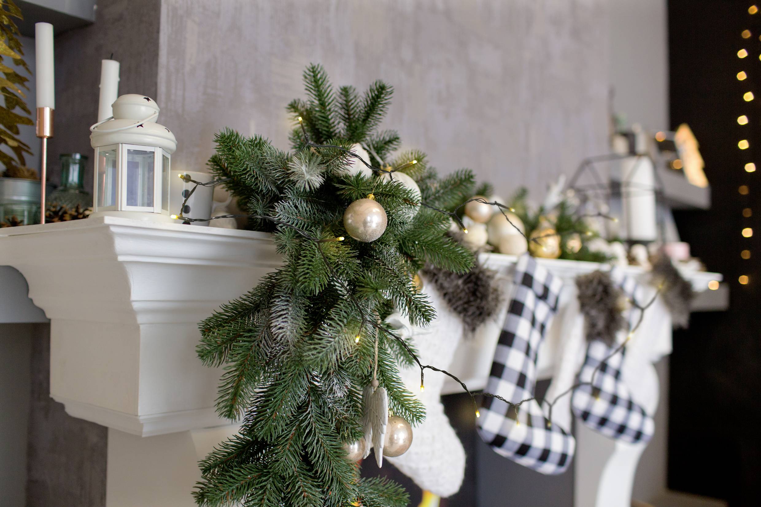 Une cheminée décorée avec une guirlande de sapin, une chaîne lumineuse et des chaussettes de Noël à motif à carreaux crée une atmosphère festive.