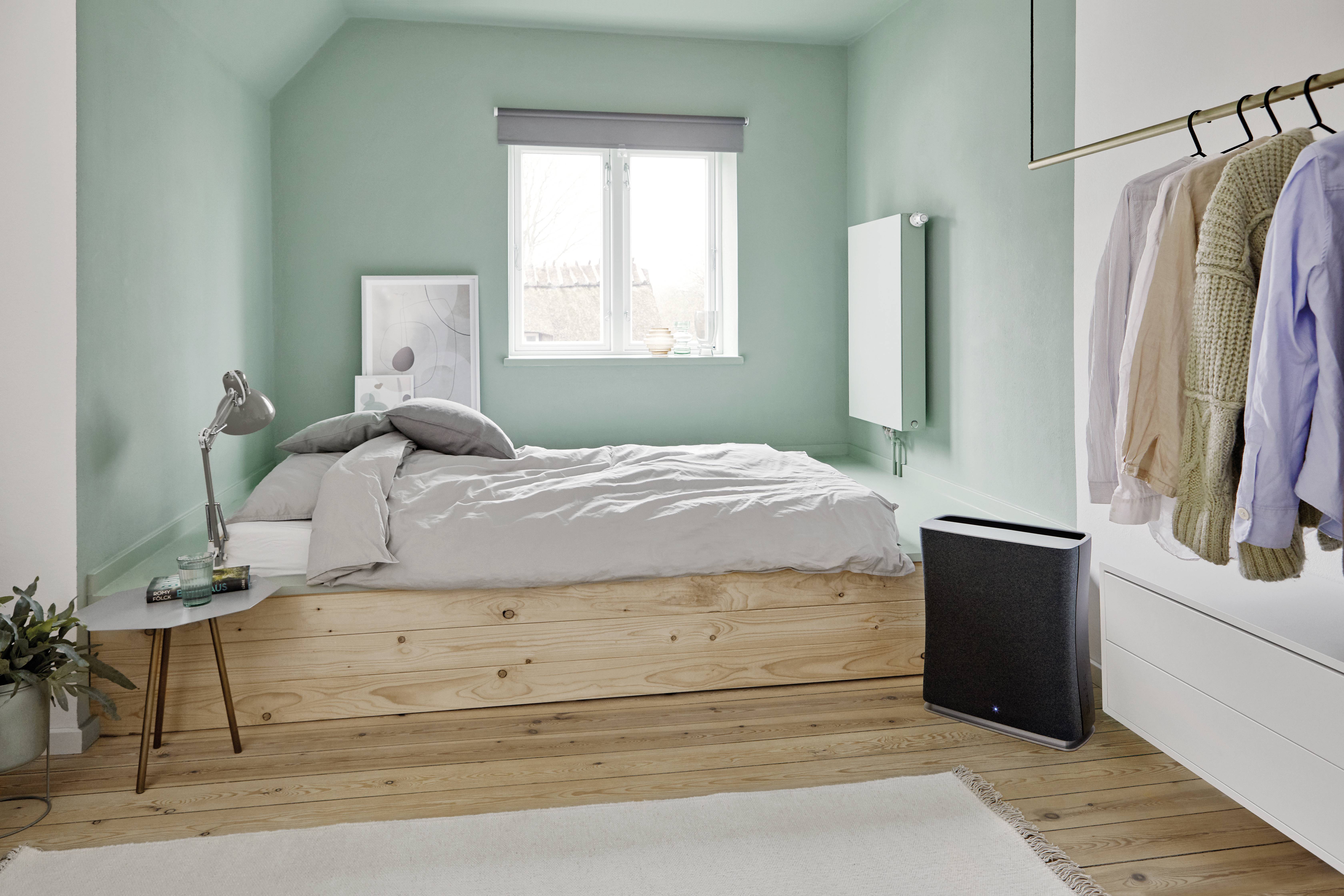 Chambre claire aux murs vert menthe, avec un lit double en bois, une tringle à vêtements fixée au mur et une fenêtre laissant entrer la lumière.