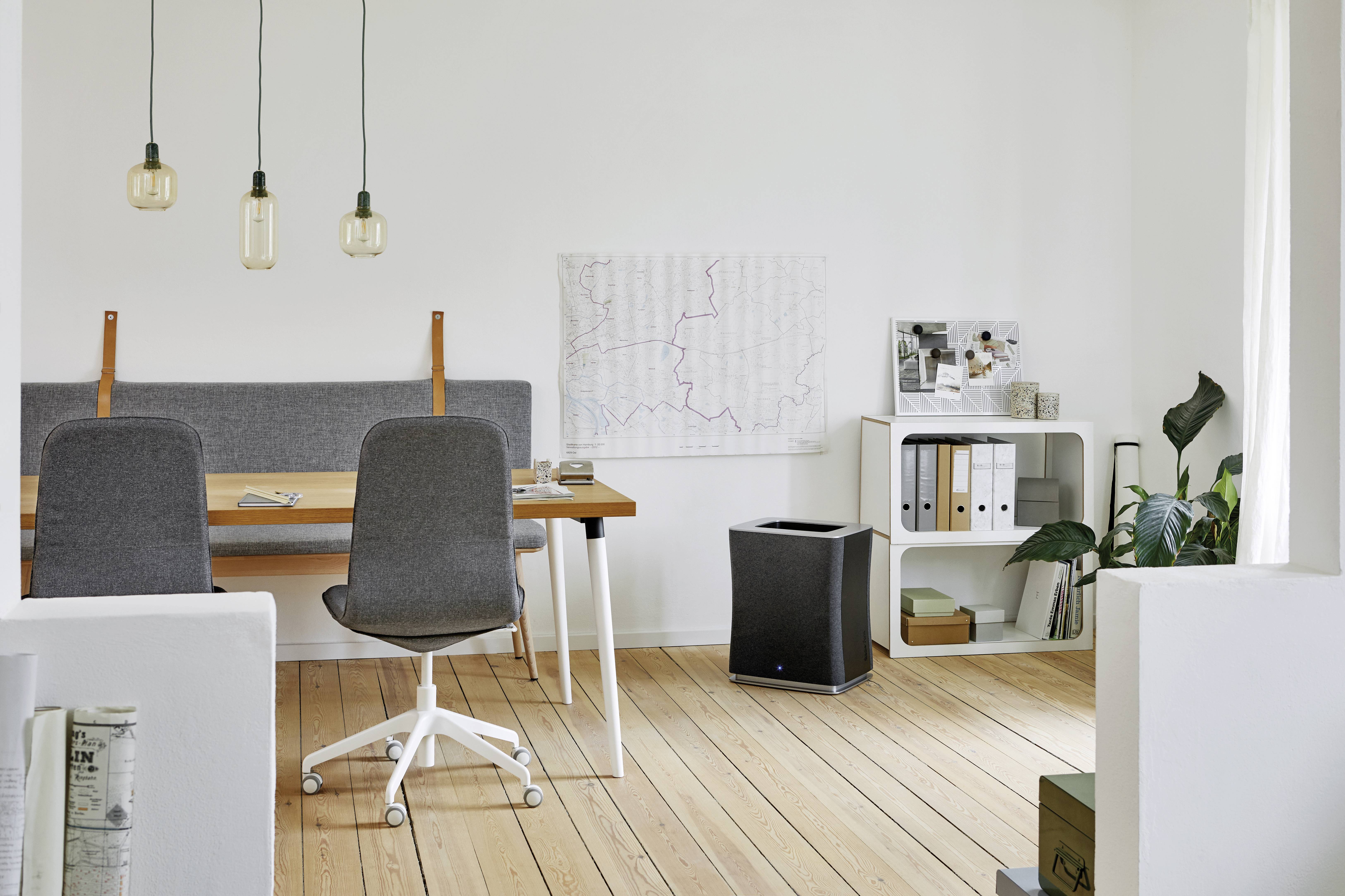 Espace de bureau moderne avec sol en bois, deux chaises grises autour d'une table, affiches au mur, étagère avec classeurs et plantes dans la pièce.