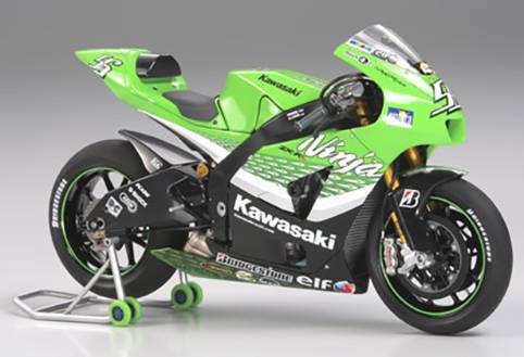 Une moto de course Kawasaki verte est posée sur un support, prête pour une course. Elle est décorée d'autocollants publicitaires et porte un numéro de course sur sa carrosserie.
