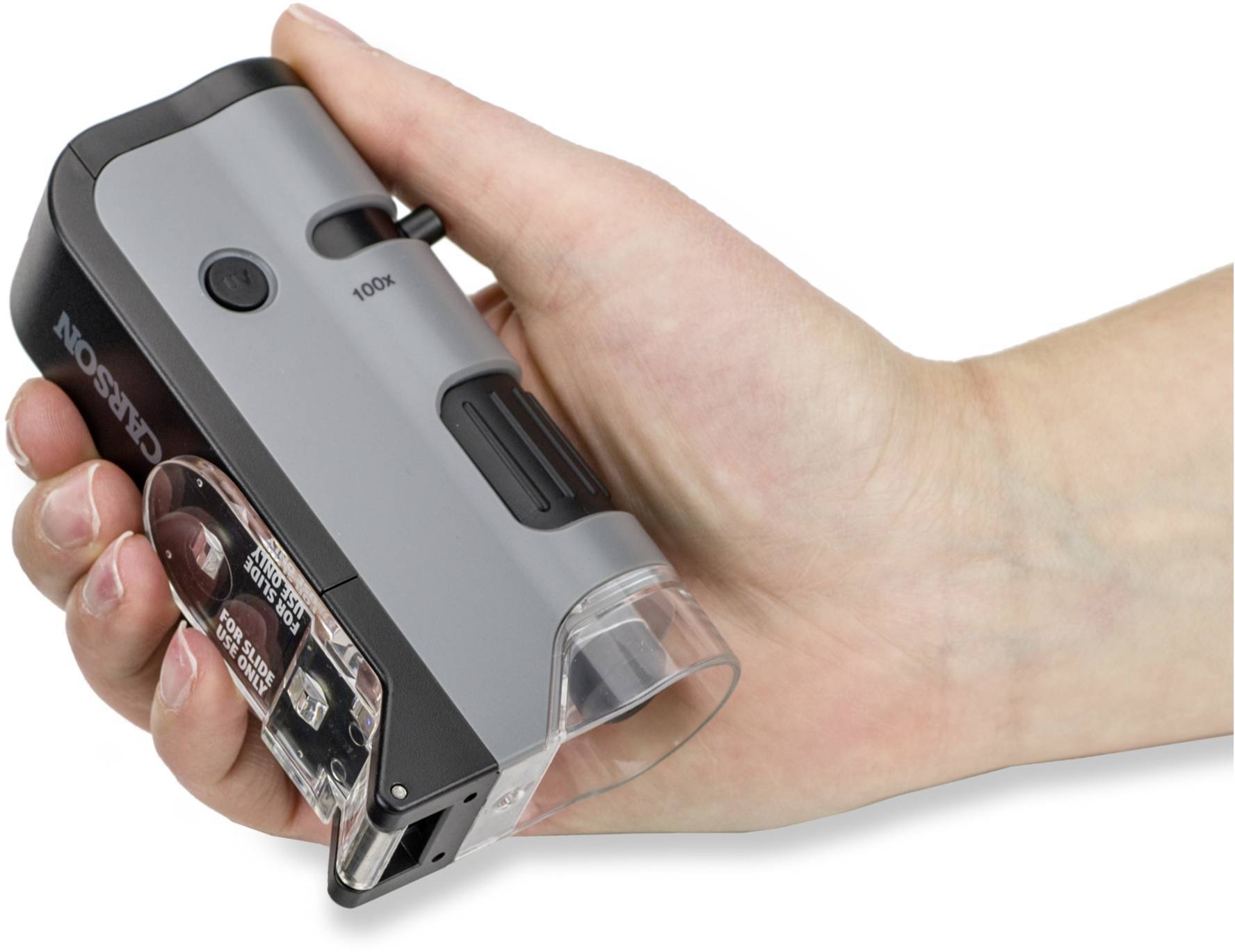 Une main tient un microscope portable au boîtier gris avec un grossissement de 100x, adapté pour l'observation rapide de petits objets.