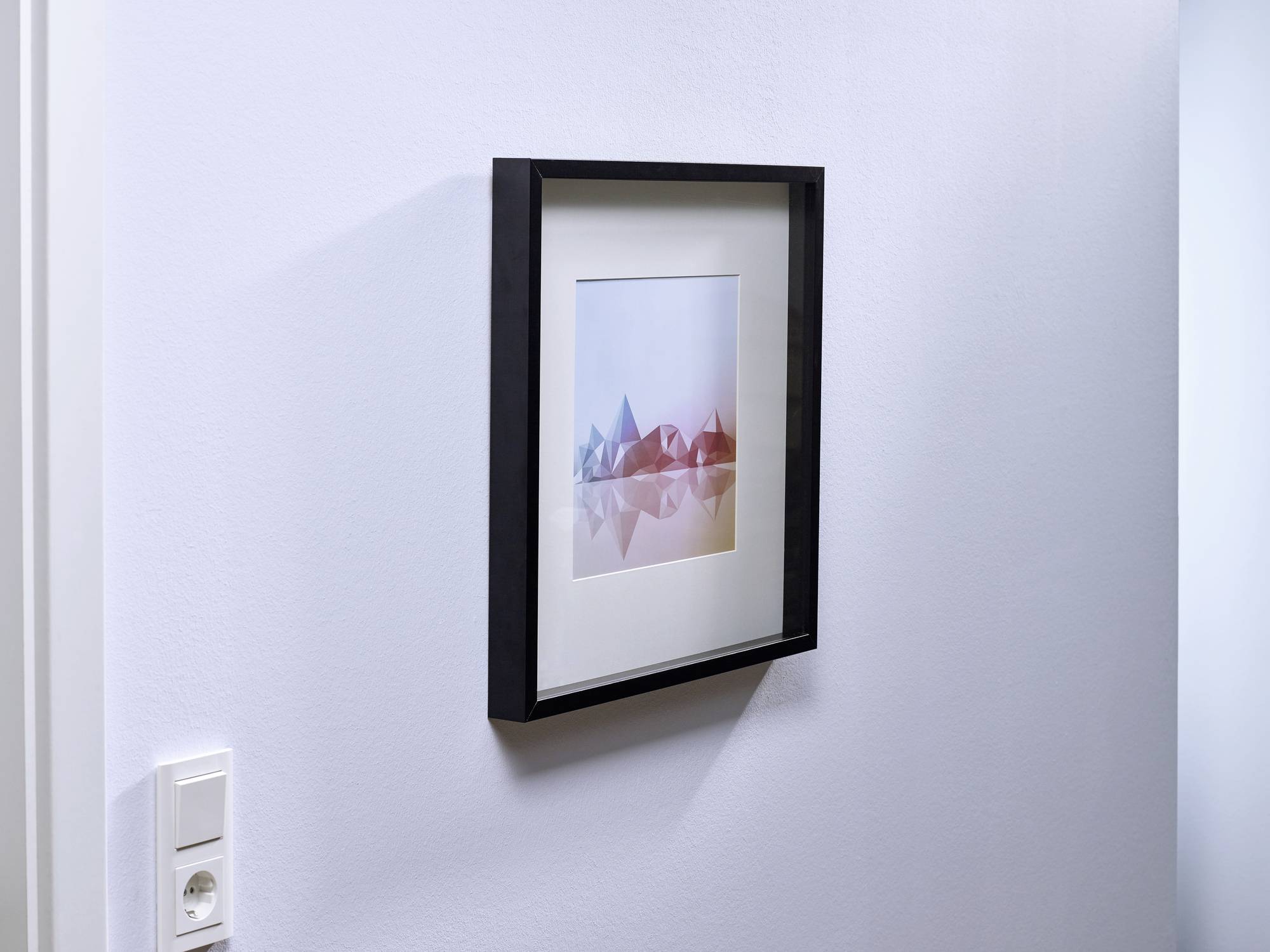 Œuvre d'art encadrée sur un mur blanc. Formes géométriques abstraites en nuances de bleu et de rouge. Interrupteur visible en bas à gauche.