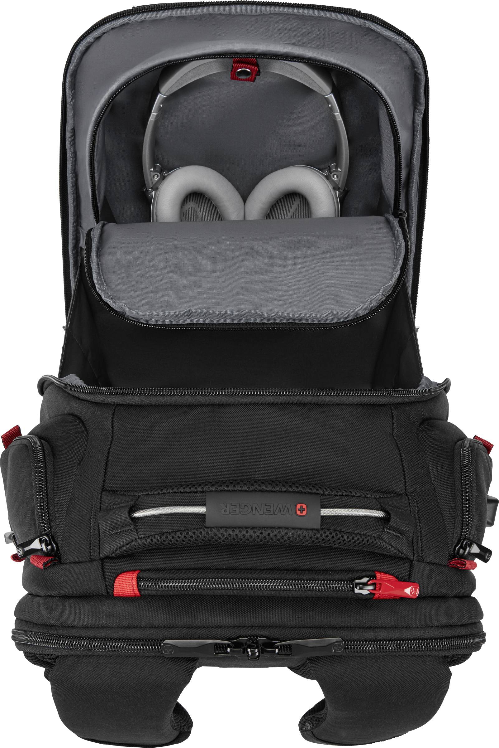 Un sac à dos noir avec des compartiments ouverts montrant des écouteurs et des accessoires électroniques. Touches de rouge et plusieurs poches à fermeture éclair.