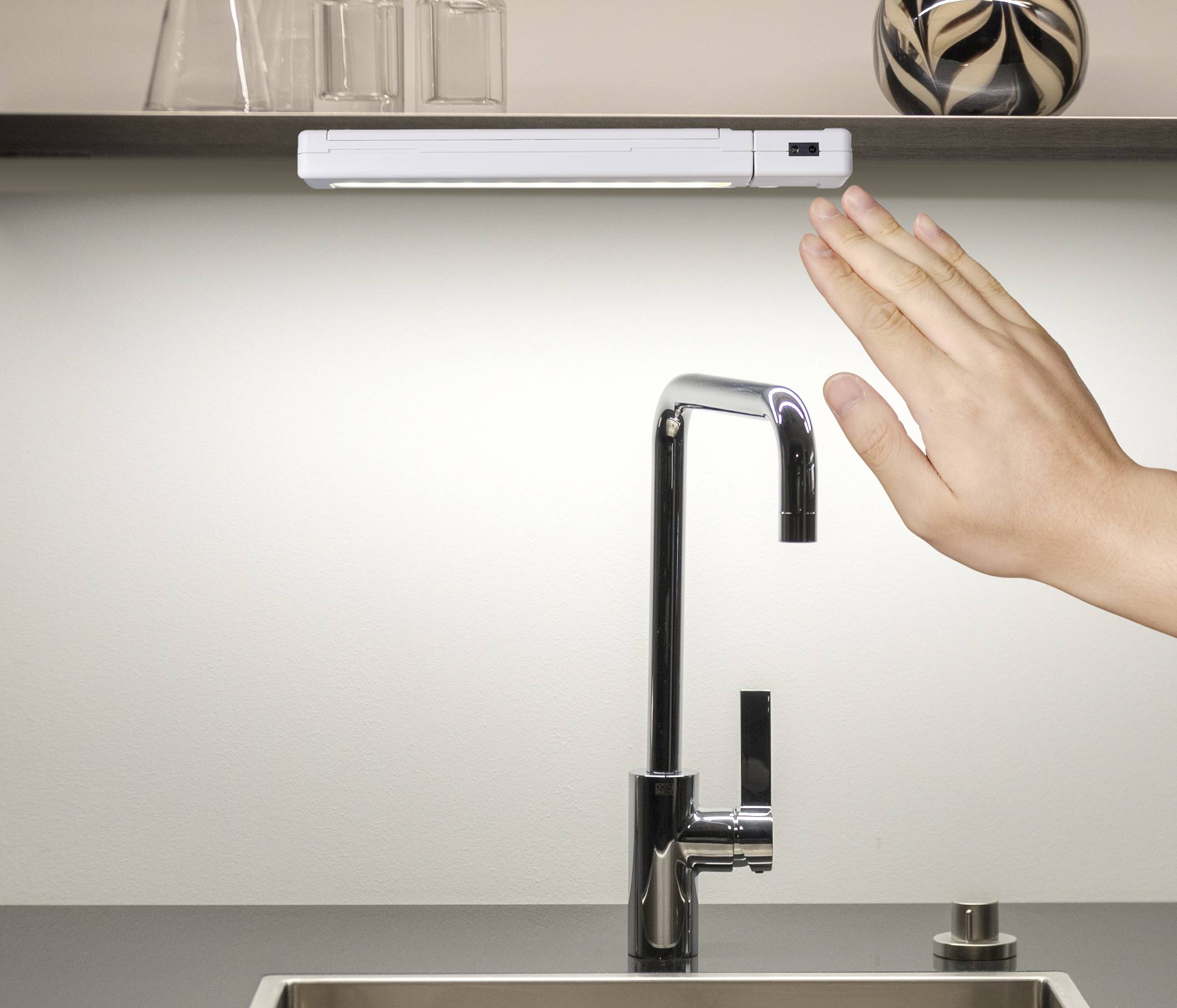 Une main se déplace au-dessus d'un robinet de cuisine moderne, probablement pour activer le robinet sans contact.