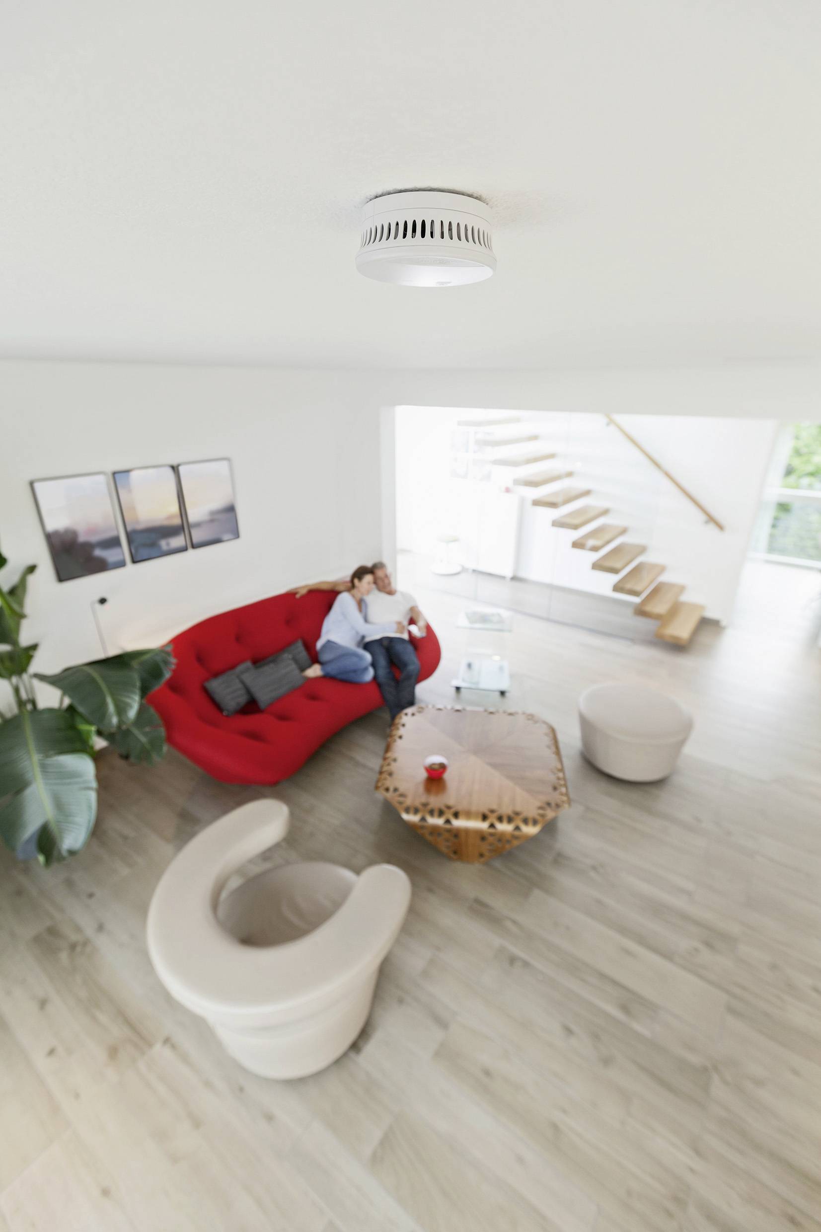 Salon avec un canapé rouge, deux fauteuils et une table basse. Des personnes sont assises sur le canapé. Décoration moderne et lumineuse.