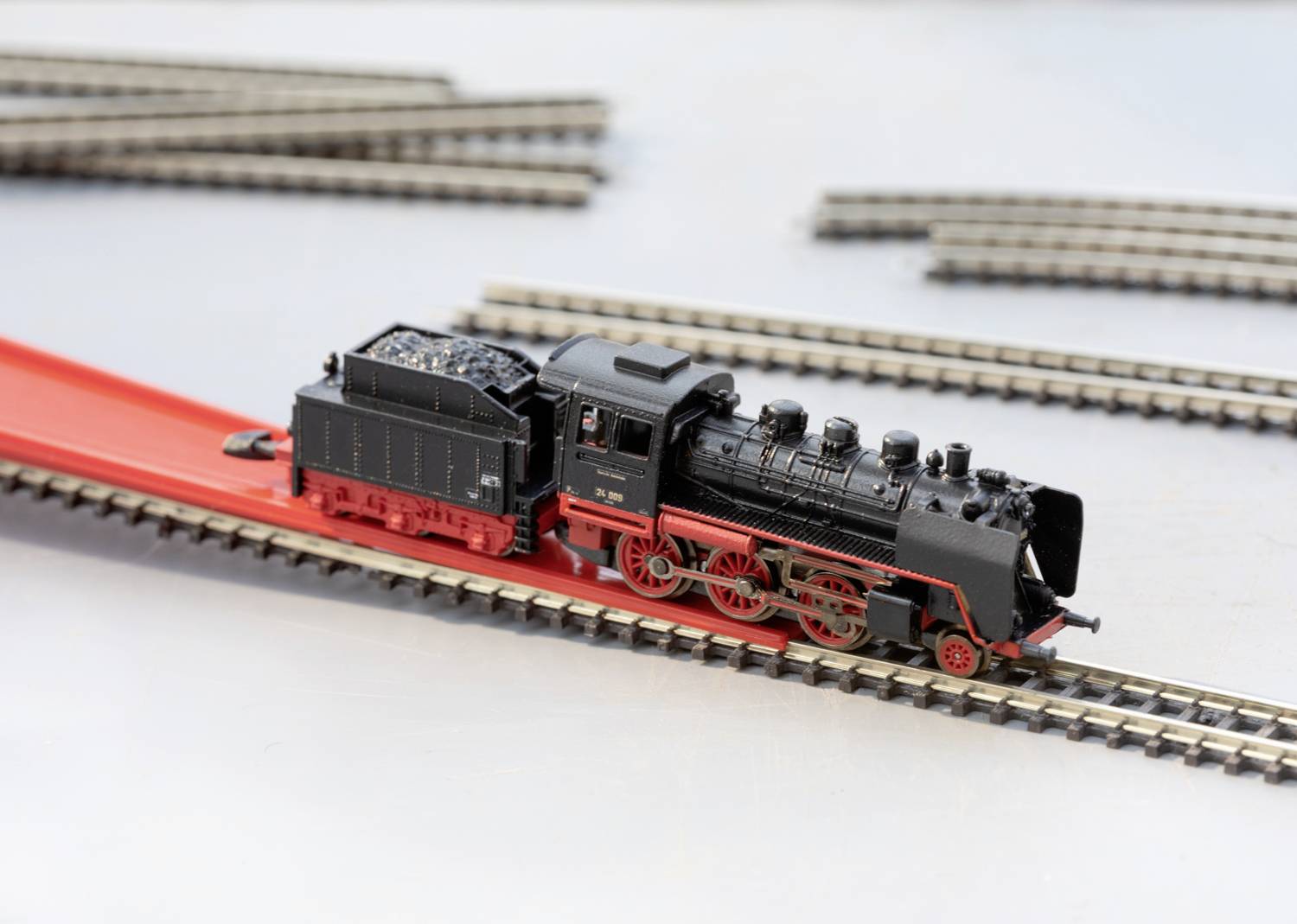 Une locomotive-modèle noire avec un châssis rouge est posée sur une voie ferrée. D'autres voies ferrées sont visibles en arrière-plan.