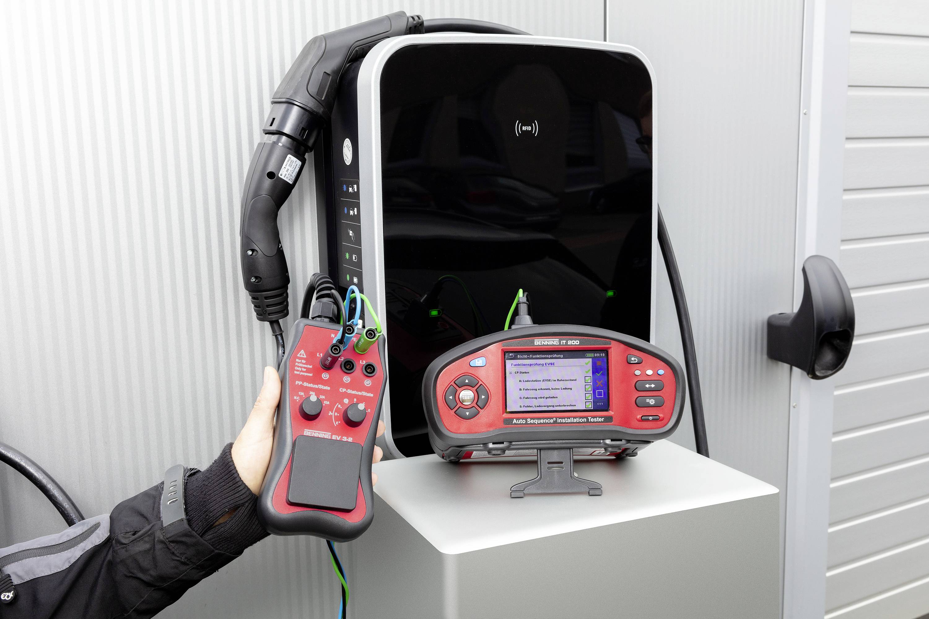 Un chargeur pour véhicules électriques est testé avec un appareil de contrôle. Une main tient l'appareil de contrôle qui affiche des résultats.
