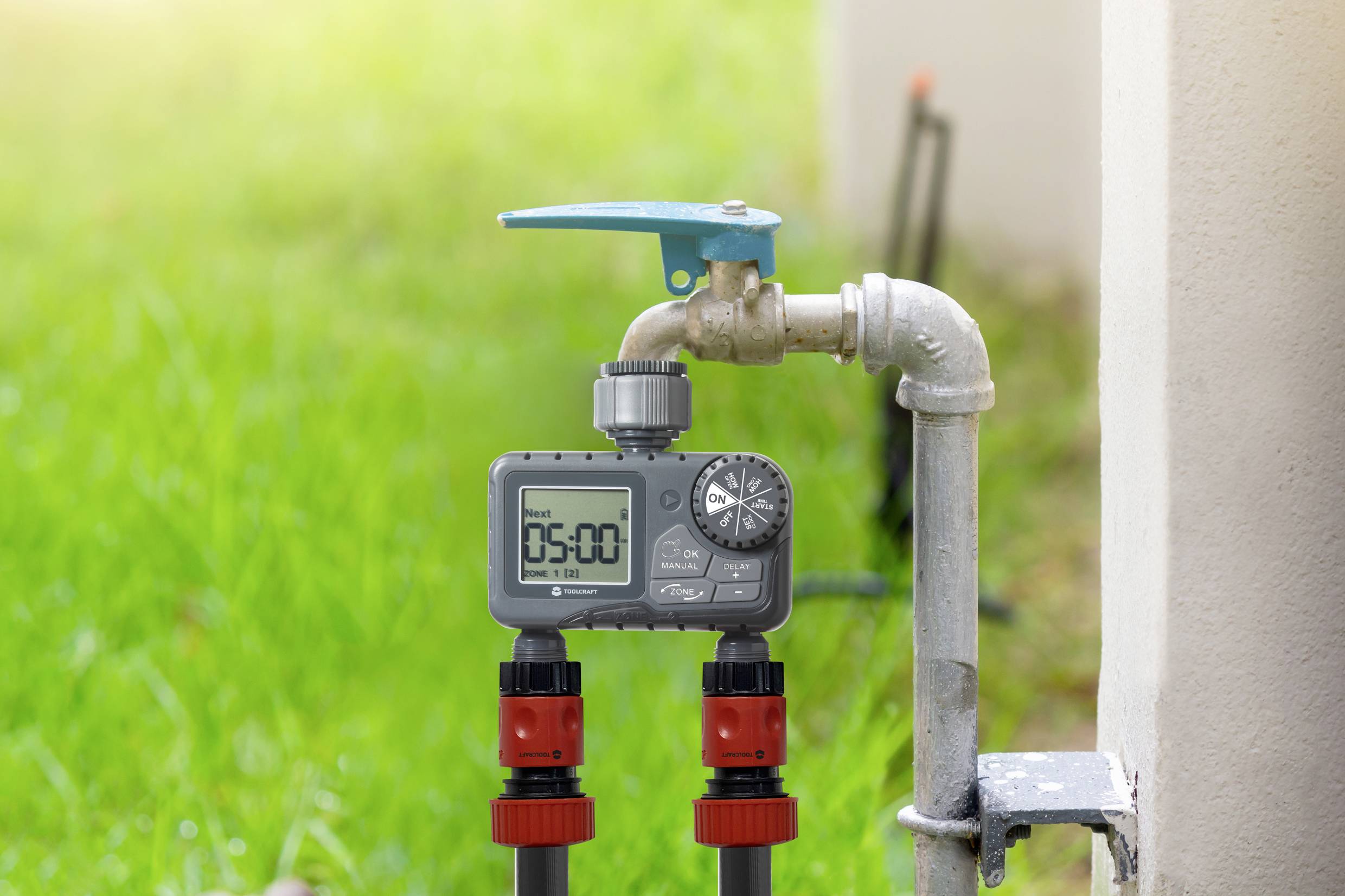 Un minuteur d'irrigation numérique est fixé à un robinet extérieur. Le timer affiche '05:00'. De l'herbe est visible en arrière-plan.