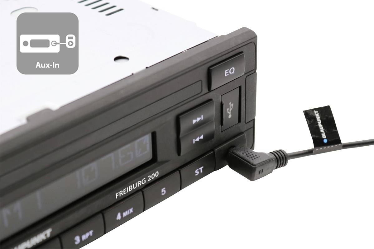 Autoradio avec port USB et câble branché, touche EQ visible. L'écran affiche le texte 'FREIBURG 200'.