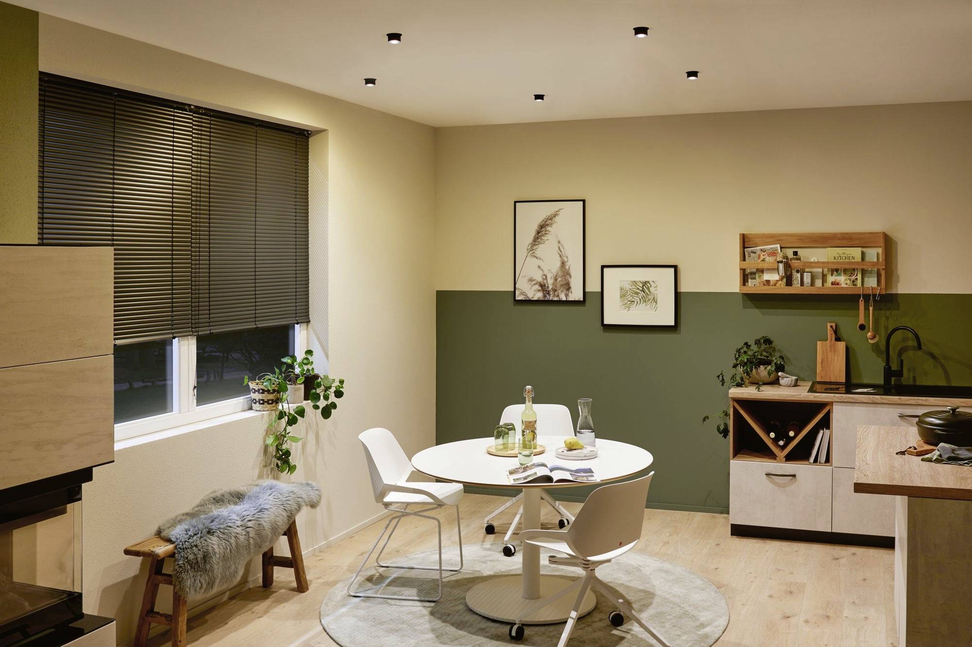 Cuisine accueillante avec table à manger, quatre chaises et plantes. Des tableaux sont accrochés au mur. Décoration intérieure moderne de style scandinave.