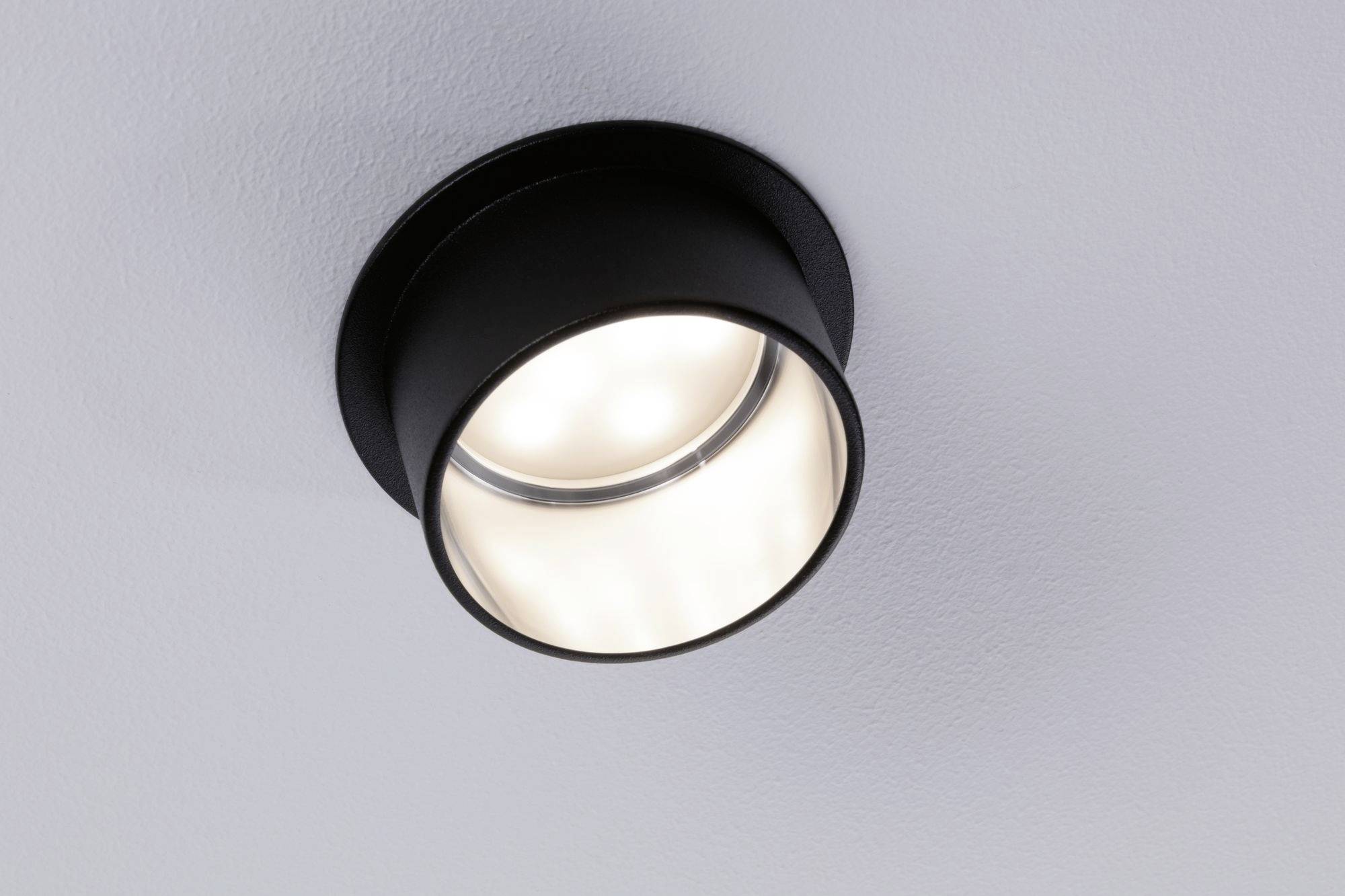 Une simple lampe de plafond noire est allumée et projette une lumière chaleureuse sur un plafond blanc.