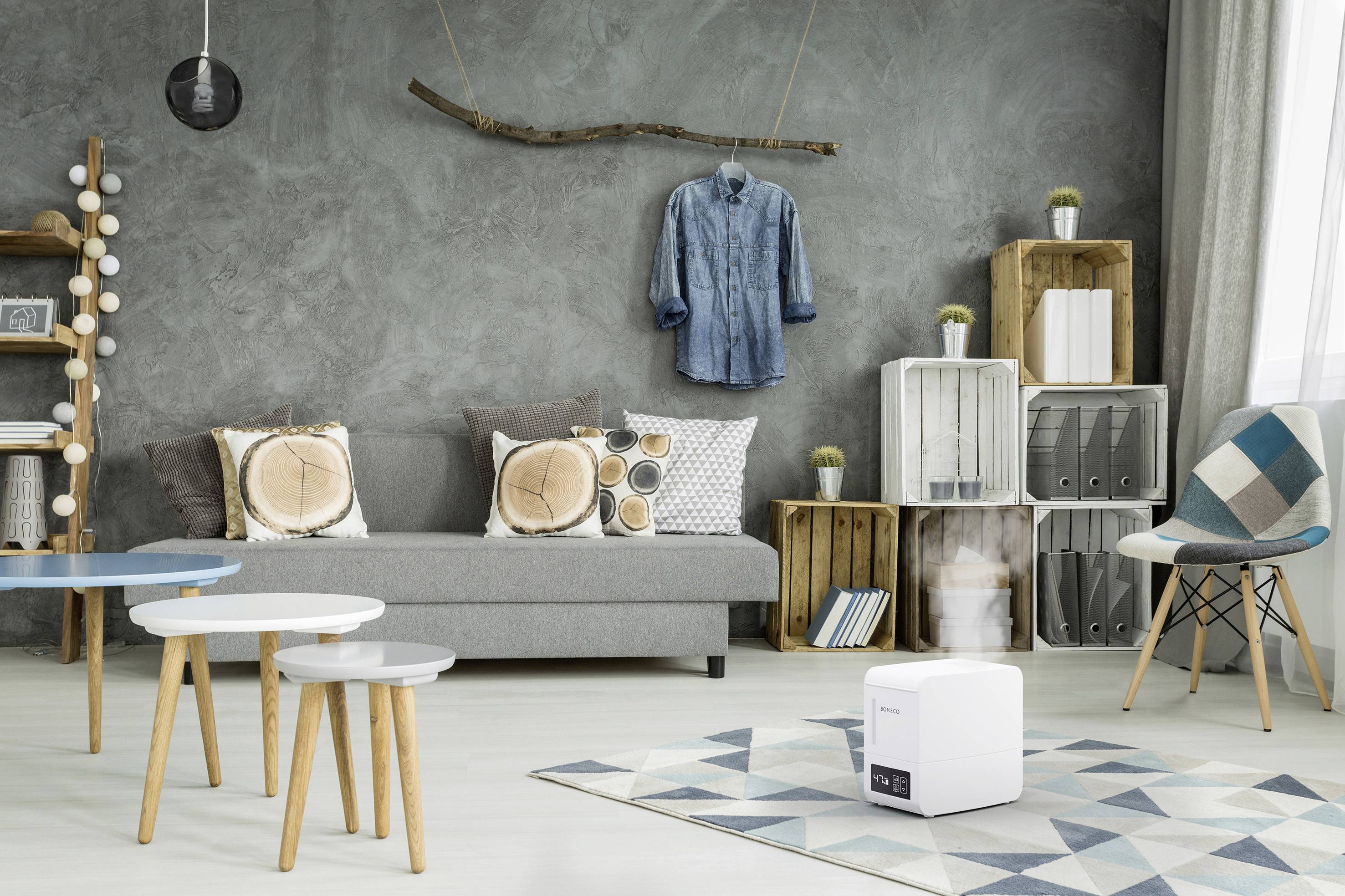 Salon moderne avec canapé gris, coussins décoratifs, chemise en jean suspendue, étagères en bois et table d'appoint élégante. Un humidificateur est posé sur le sol.