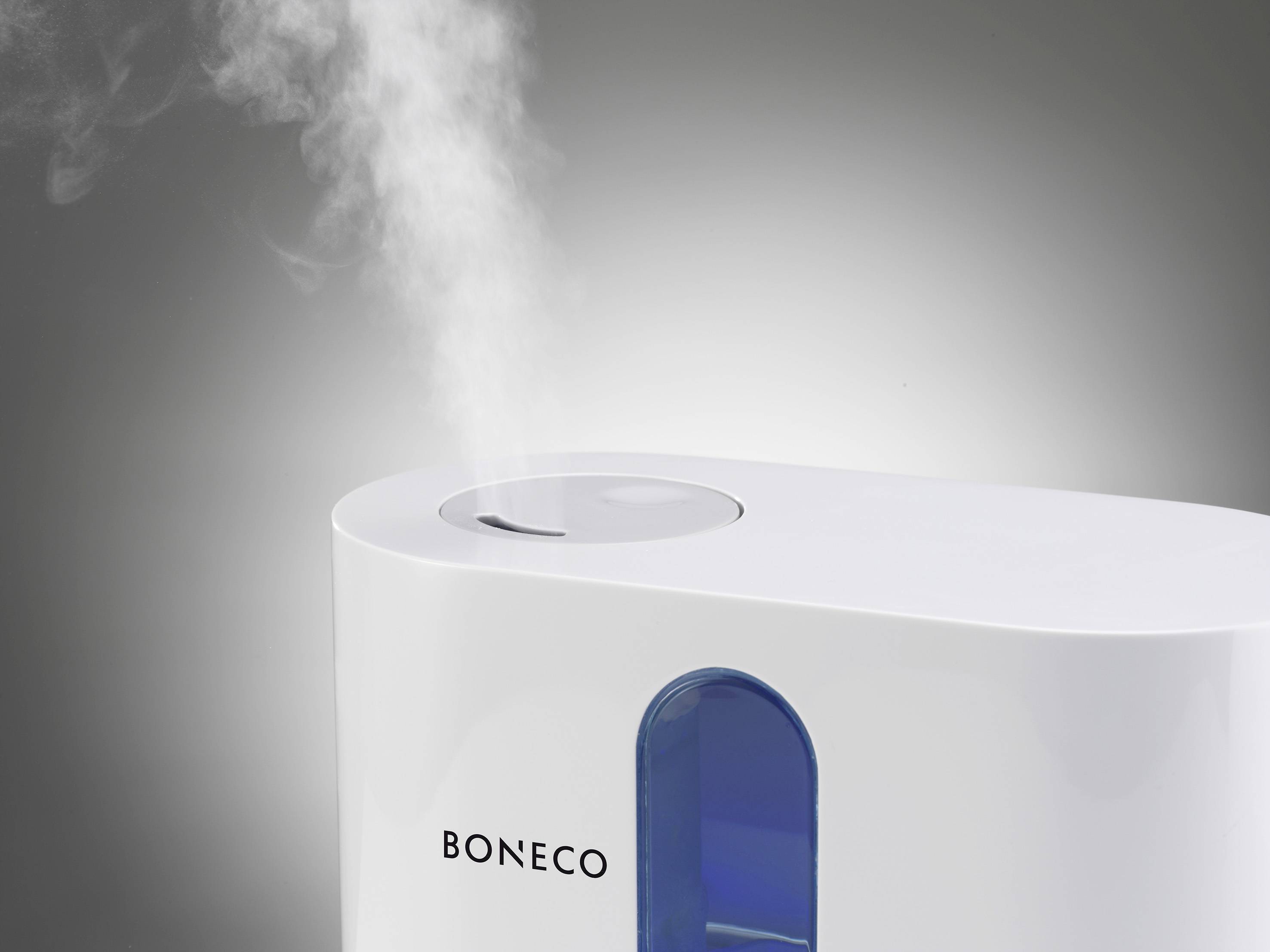 Un humidificateur blanc émet un fin flux de vapeur sur un fond gris. L'appareil dispose d'une fenêtre indiquant le niveau d'eau.