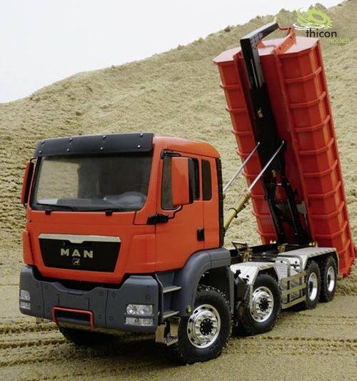Un camion rouge à benne basculante est stationné sur une colline de sable dans un environnement de chantier.
