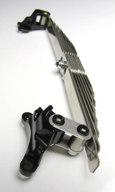 Barreau métallique avec éléments de fixation et vis sur fond blanc, probablement un composant de machine ou de véhicule.