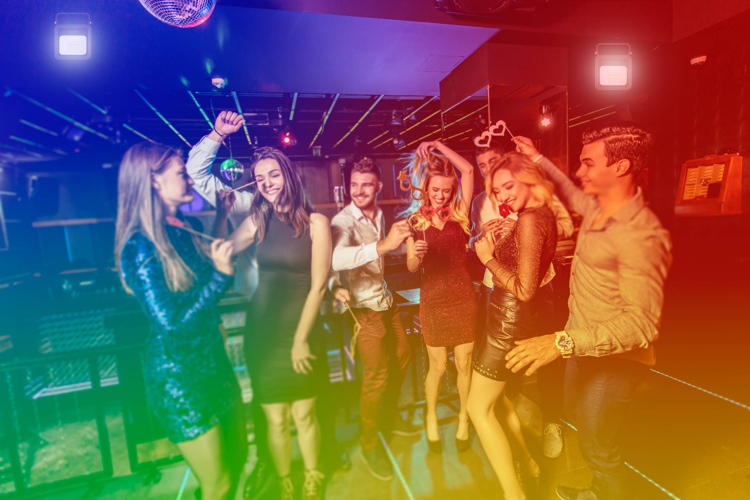 Un groupe de personnes danse et fait la fête dans un club, entouré de lumières colorées qui créent une atmosphère joyeuse et festive.