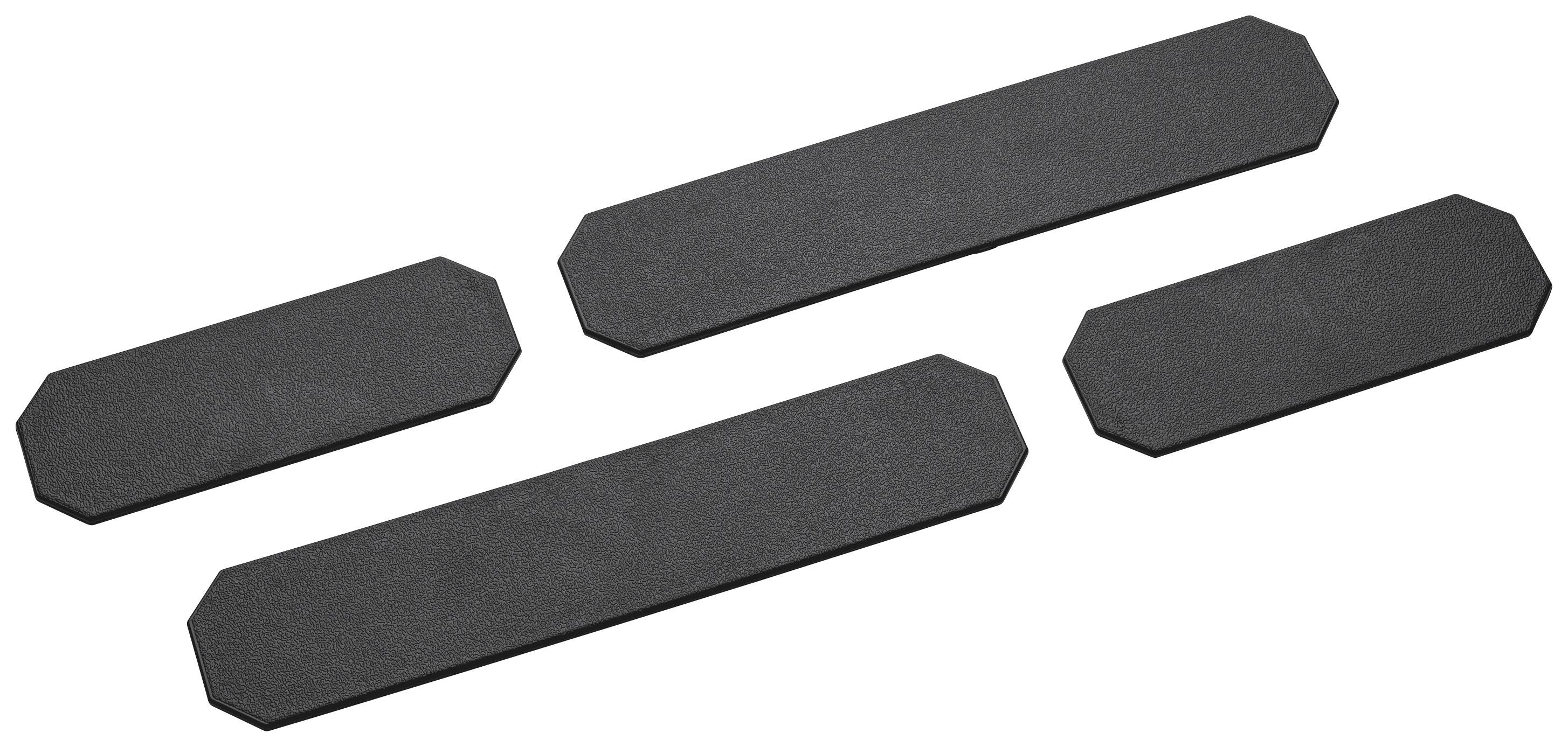 Quatre bandes adhésives noires, rectangulaires, aux coins biseautés, posées sur une surface blanche.