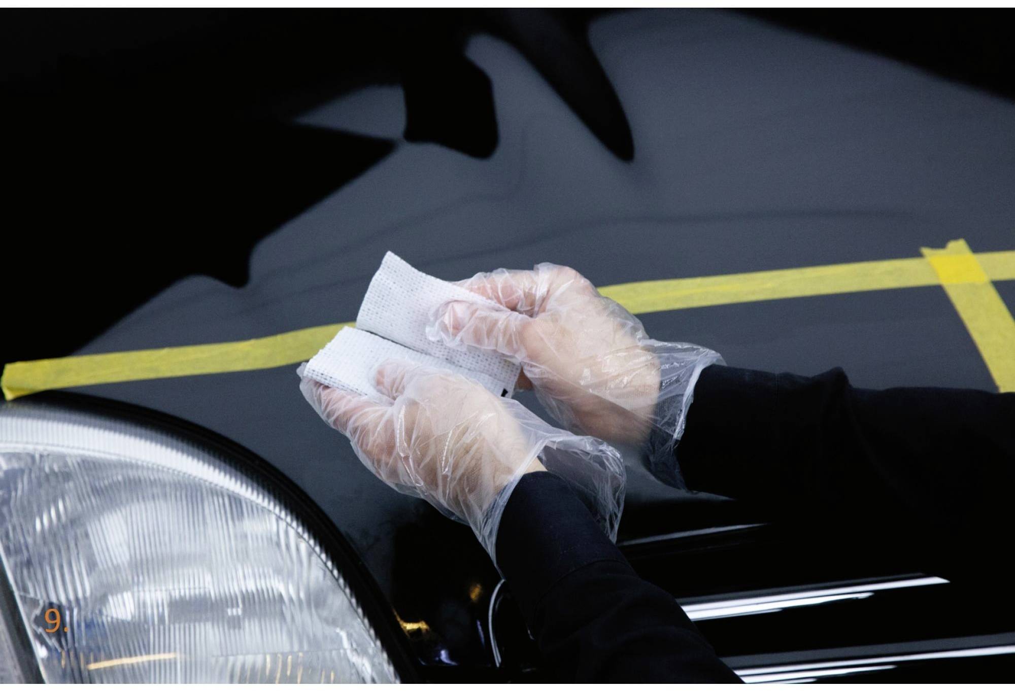Des mains gantées de gants en plastique polissent le capot d'une voiture avec un chiffon.