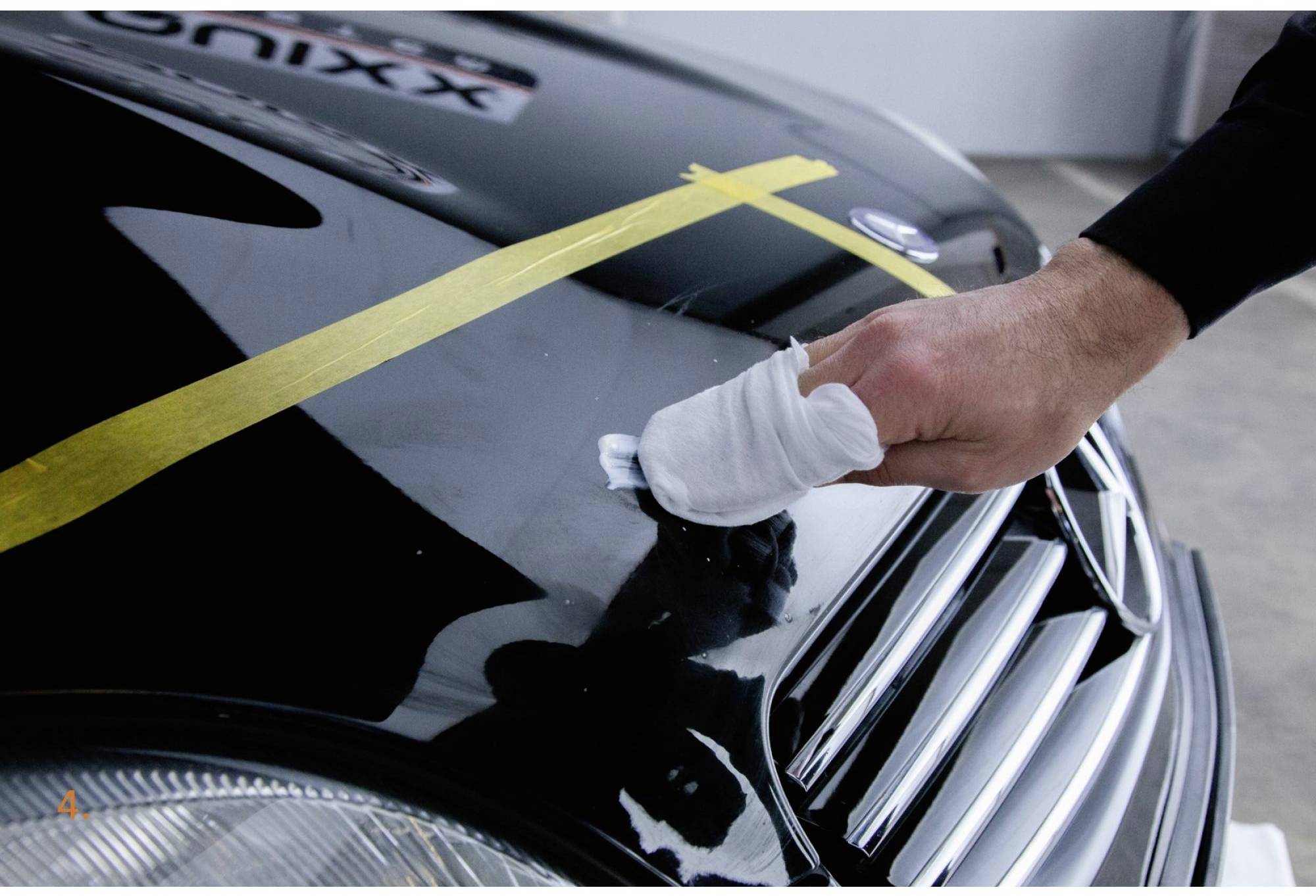 Une personne polit le vernis noir d'une voiture jusqu'à obtenir un brillant parfait en utilisant un doigt recouvert de tissu.