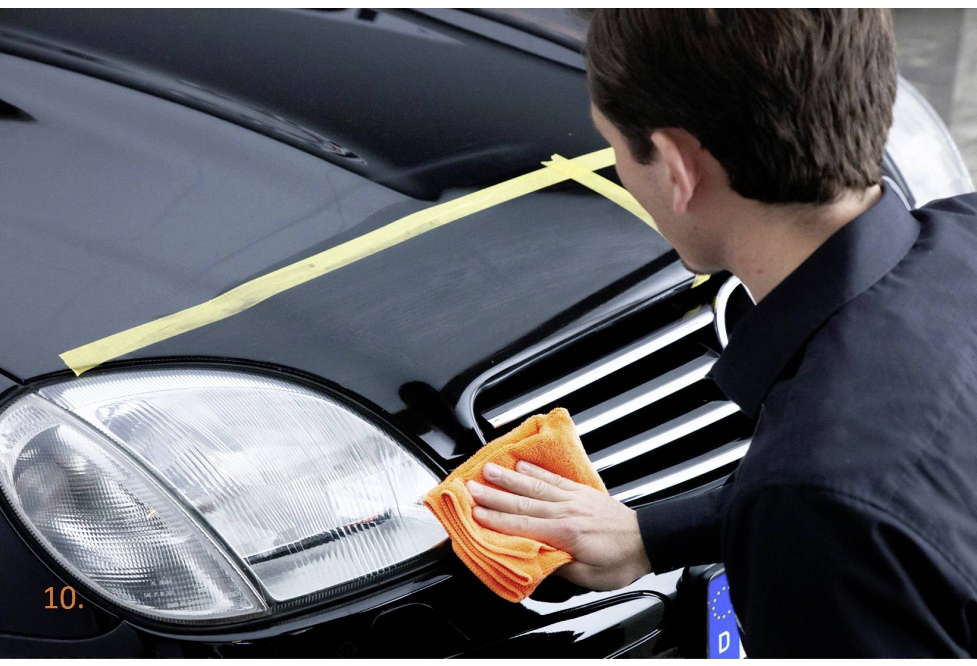 Une personne polit les phares et la calandre d'une voiture noire avec un chiffon orange.