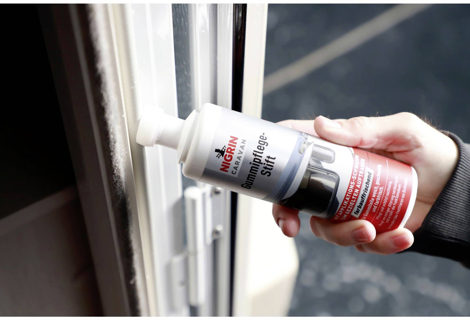 Une main tient un stylo de soin pour caoutchouc et applique le produit sur le joint d'étanchéité d'une porte. Le stylo protège contre le dessèchement.