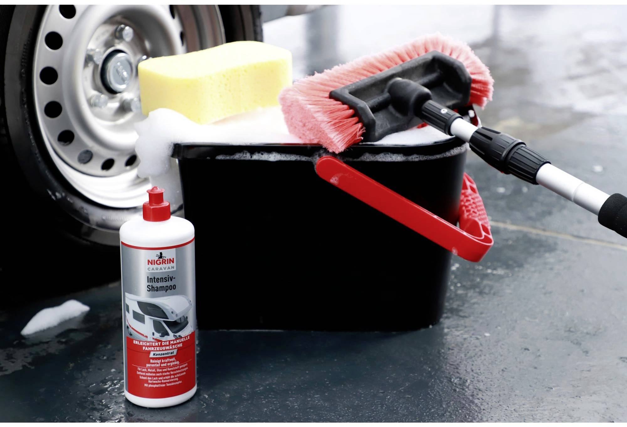 Kit de nettoyage de voiture avec bouteille de shampoing, seau noir, serpillière rouge, éponge jaune ; pneus en arrière-plan.