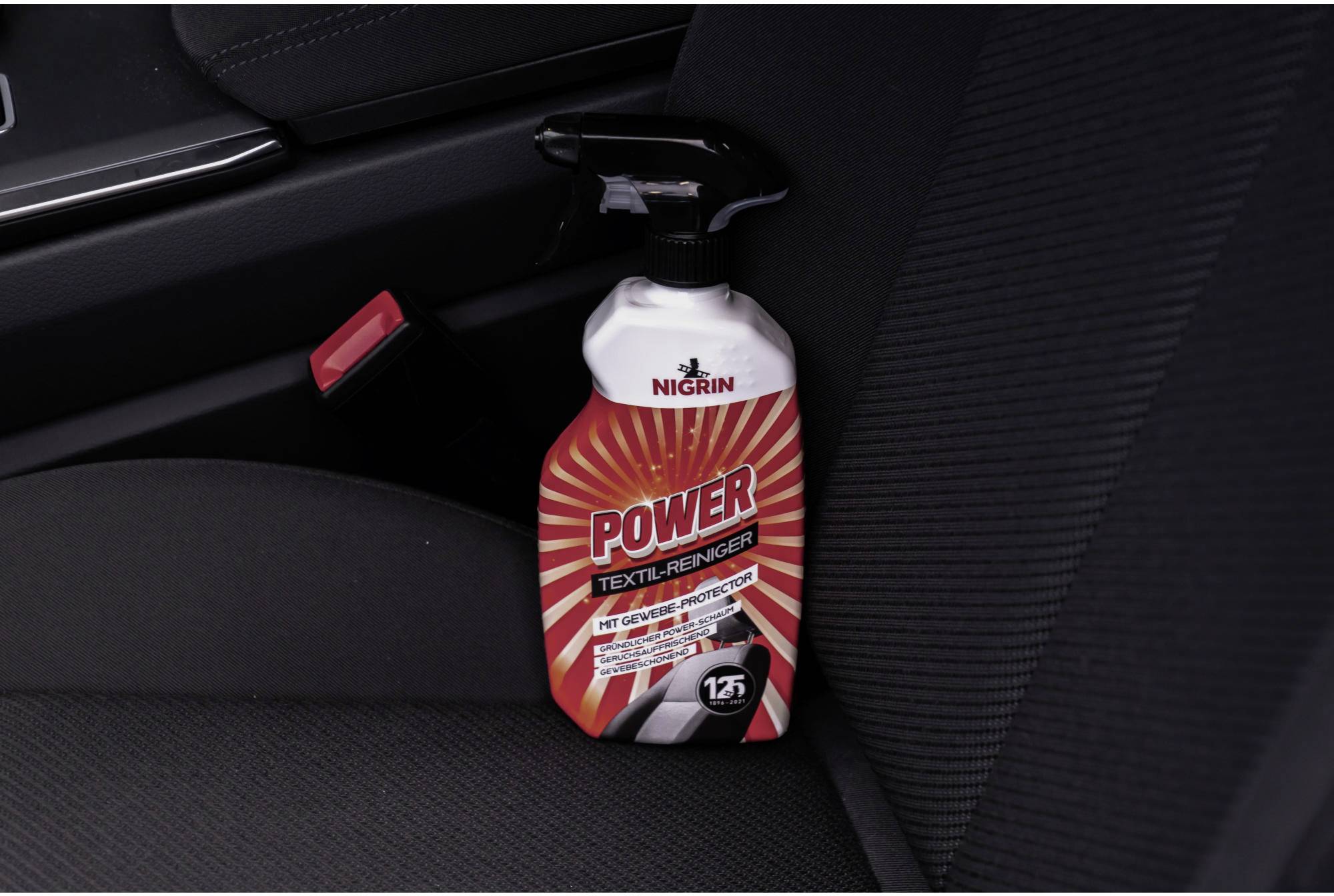 Bouteille de 'Nettoyant Textile Power' posée sur un siège de voiture, placée près d'une ceinture de sécurité. Produit de nettoyage pour intérieur automobile.