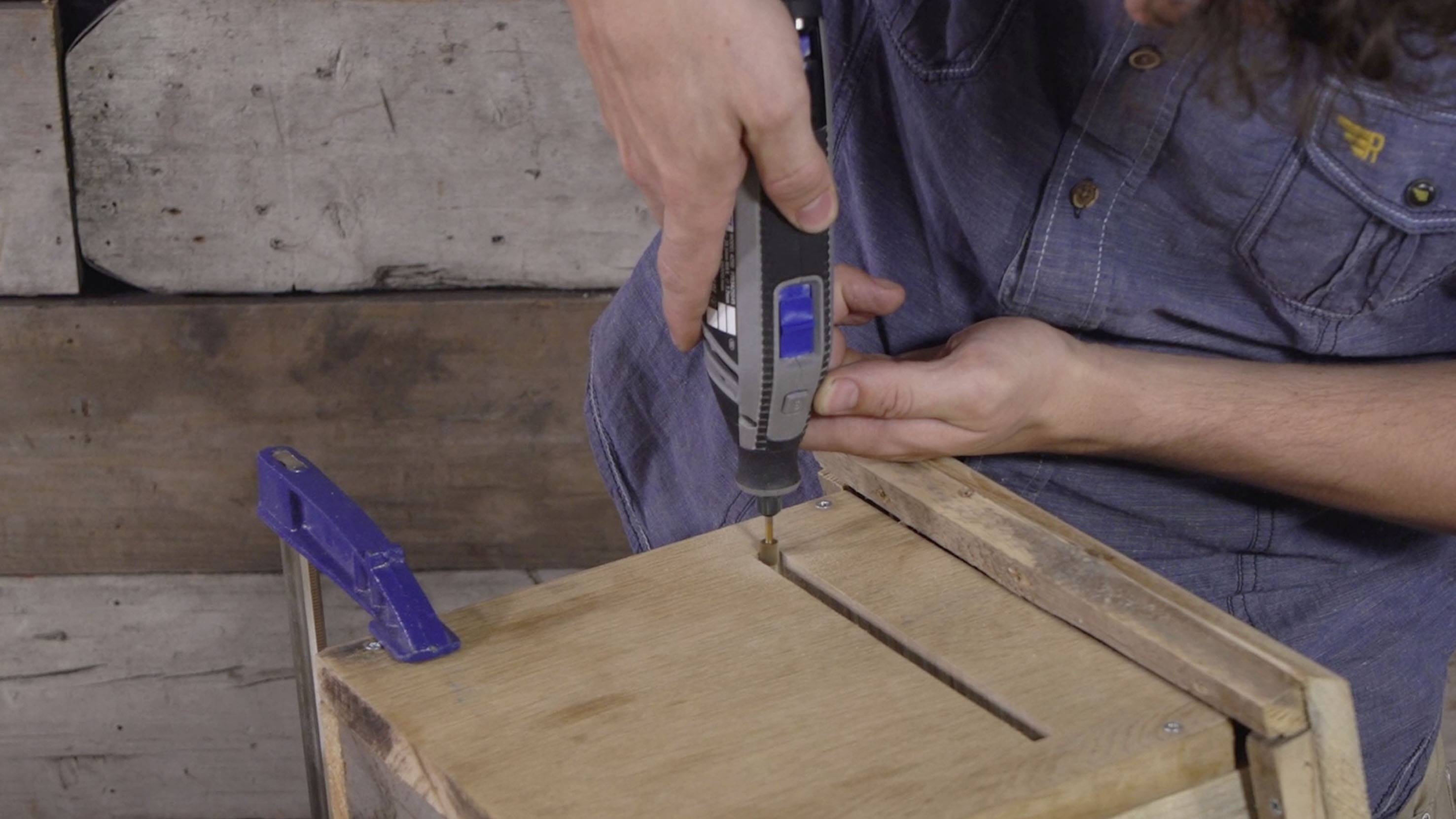 Une personne utilise un outil multifonction pour travailler un morceau de bois. Un revêtement en bois est visible en arrière-plan.