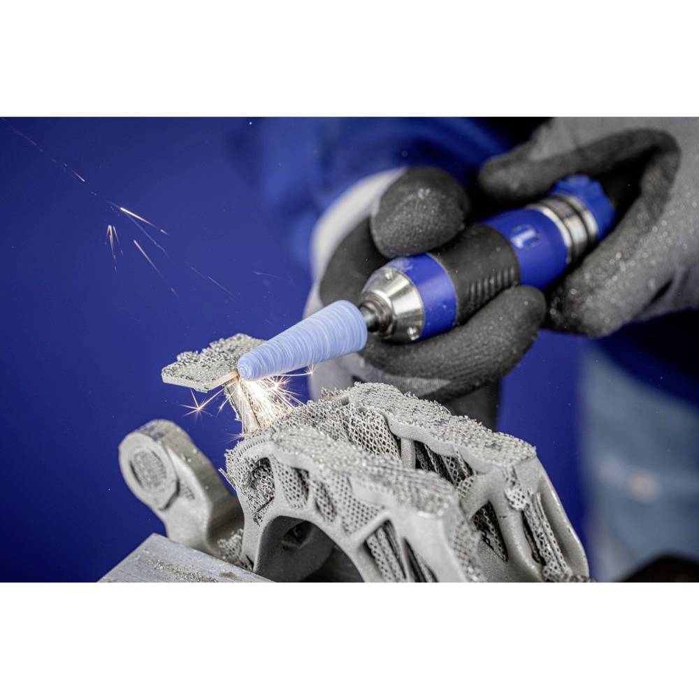 Une personne travaille avec un outil bleu sur un objet métallique imprimé en 3D. Des étincelles jaillissent pendant l'usinage.