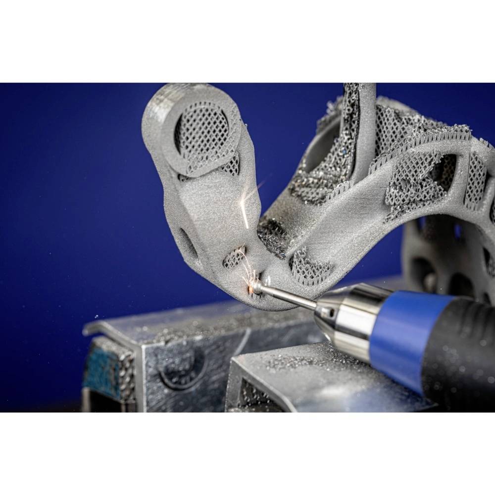 Gros plan d'un composant d'impression 3D en cours de traitement avec un outil bleu. Des étincelles jaillissent lors de l'usinage de la pièce métallique.