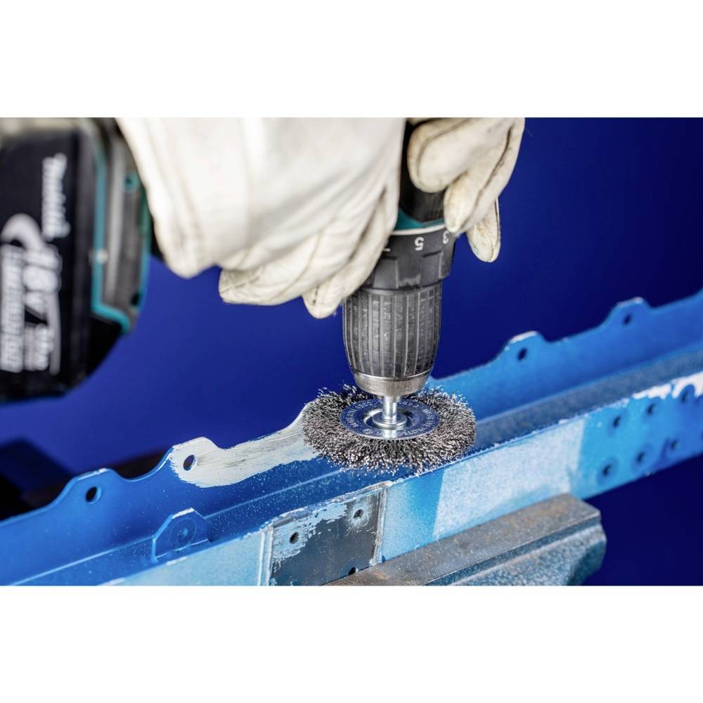 Une personne utilise une perceuse avec un accessoire de brosse métallique pour enlever la peinture d'un support métallique bleu.