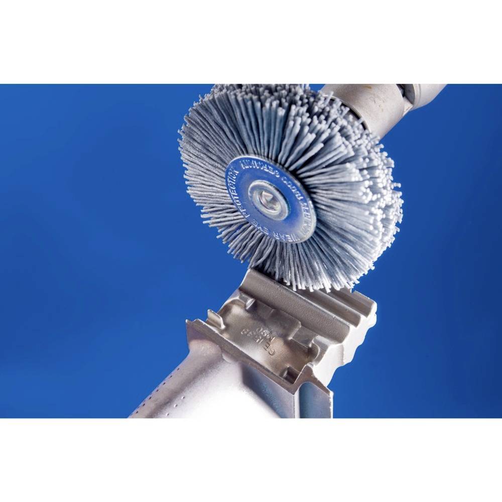 Une brosse métallique nettoie la surface d'une pièce métallique sur un fond bleu.