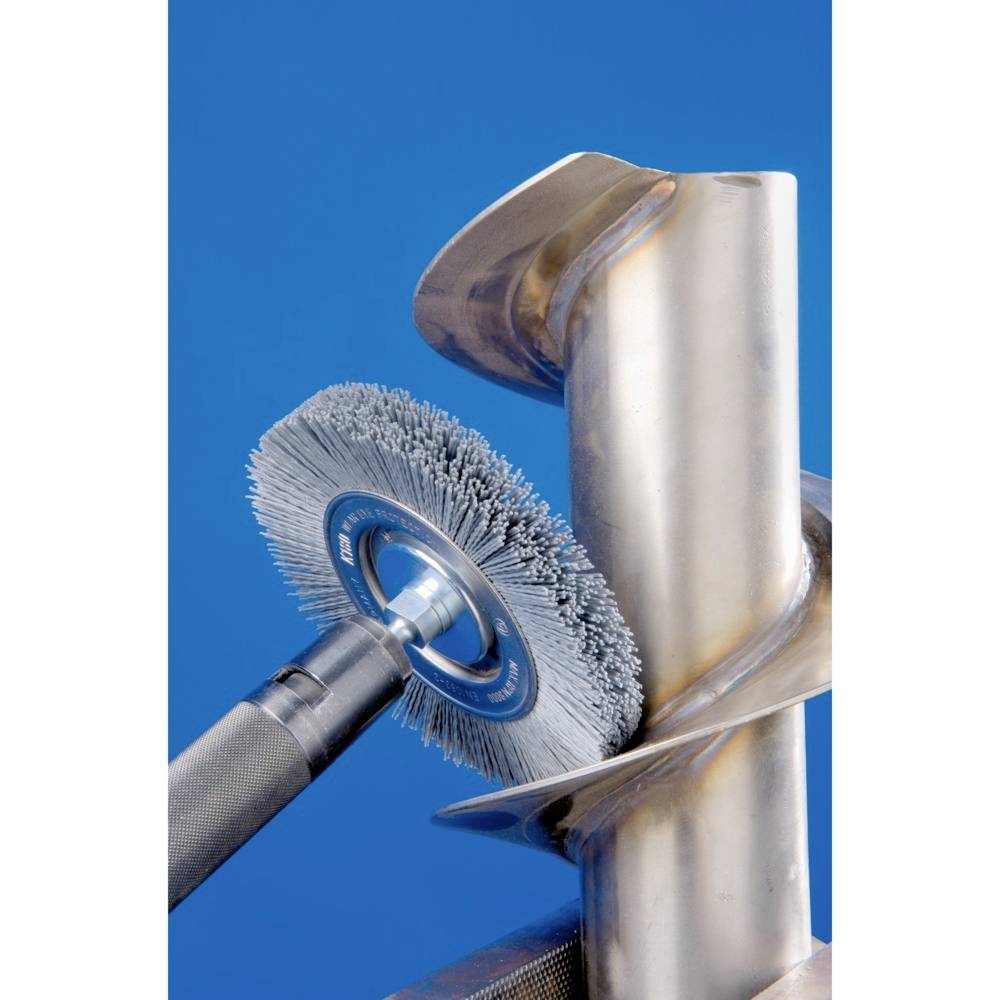 Un brosse métallique nettoie une surface métallique incurvée contre un fond bleu. La brosse présente des signes d'usure évidents.