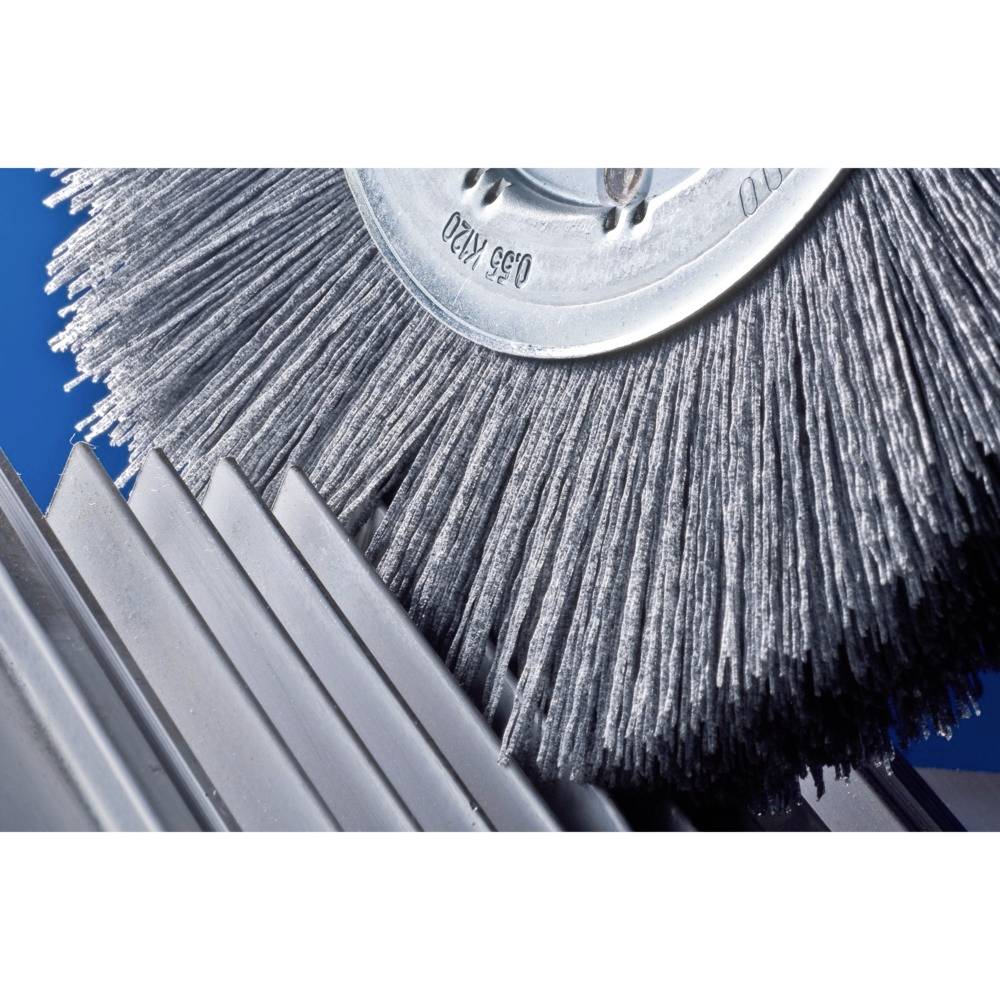 Grande brosse métallique rotative traitant des tôles métalliques. Accent sur les poils et la surface métallique réfléchissante.