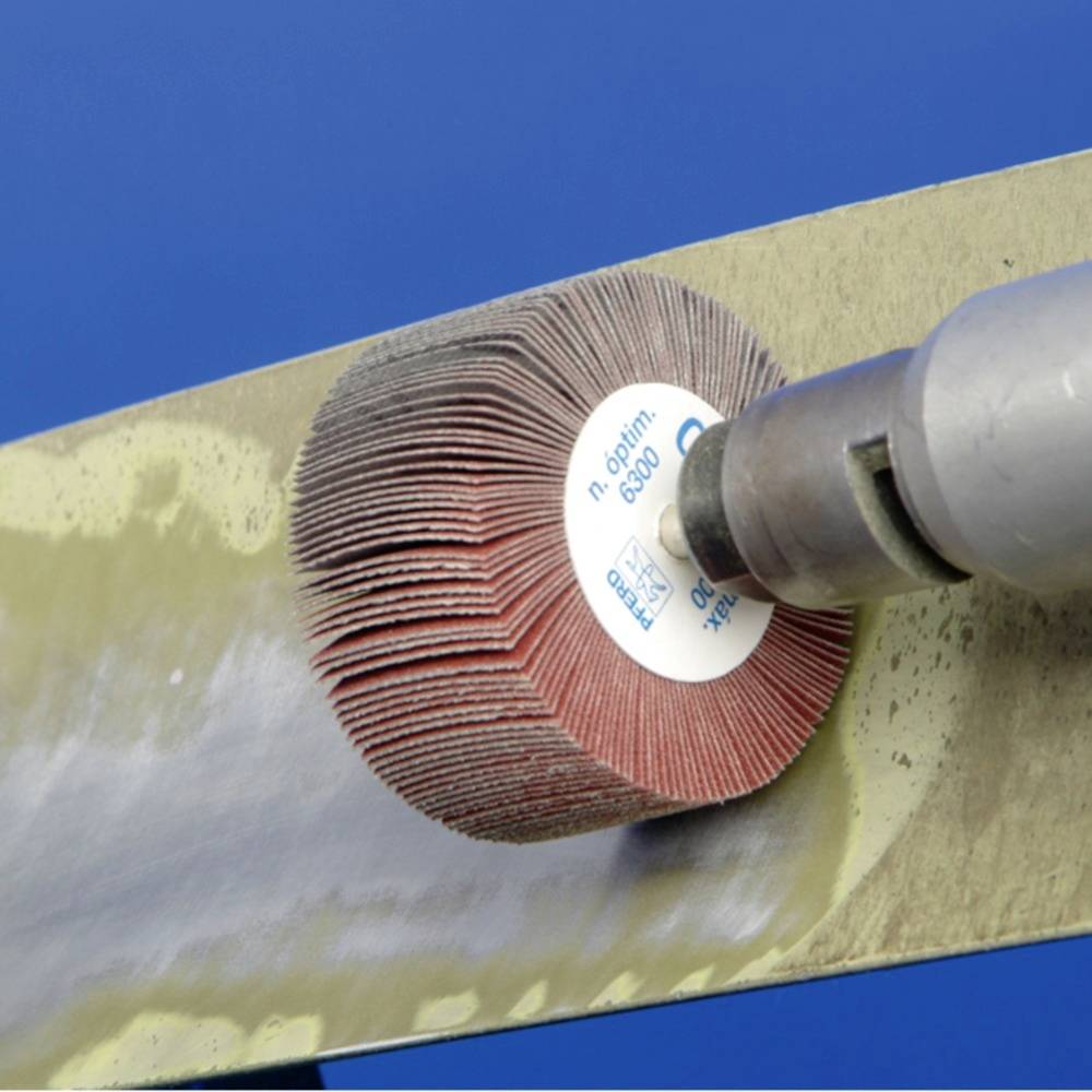 Une meule rotative à lamelles ponce une surface métallique et produit une surface lisse et polie.