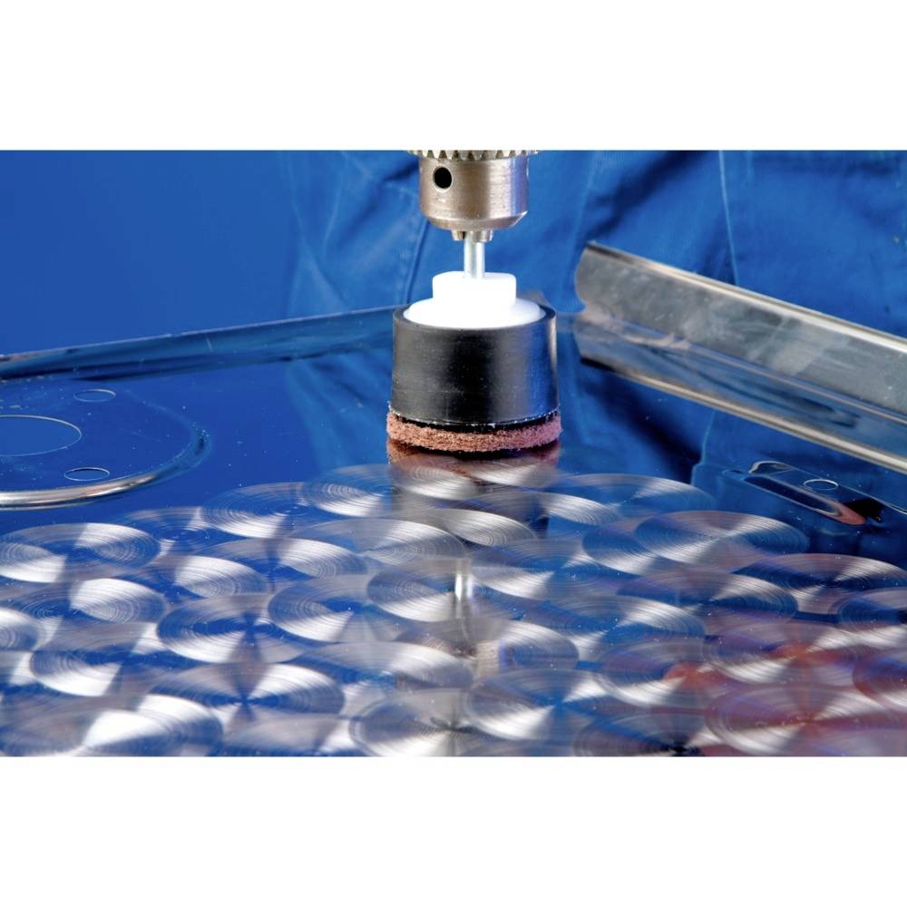 Une machine polit une surface métallique présentant des motifs circulaires. Un capuchon en plastique sur l'accessoire de polissage empêche les dommages.