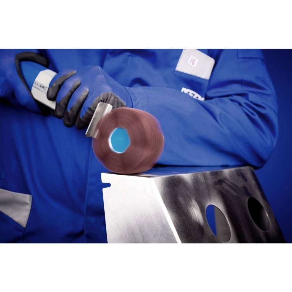 Une personne vêtue de vêtements de travail bleus polit une surface métallique avec un disque abrasif rouge.