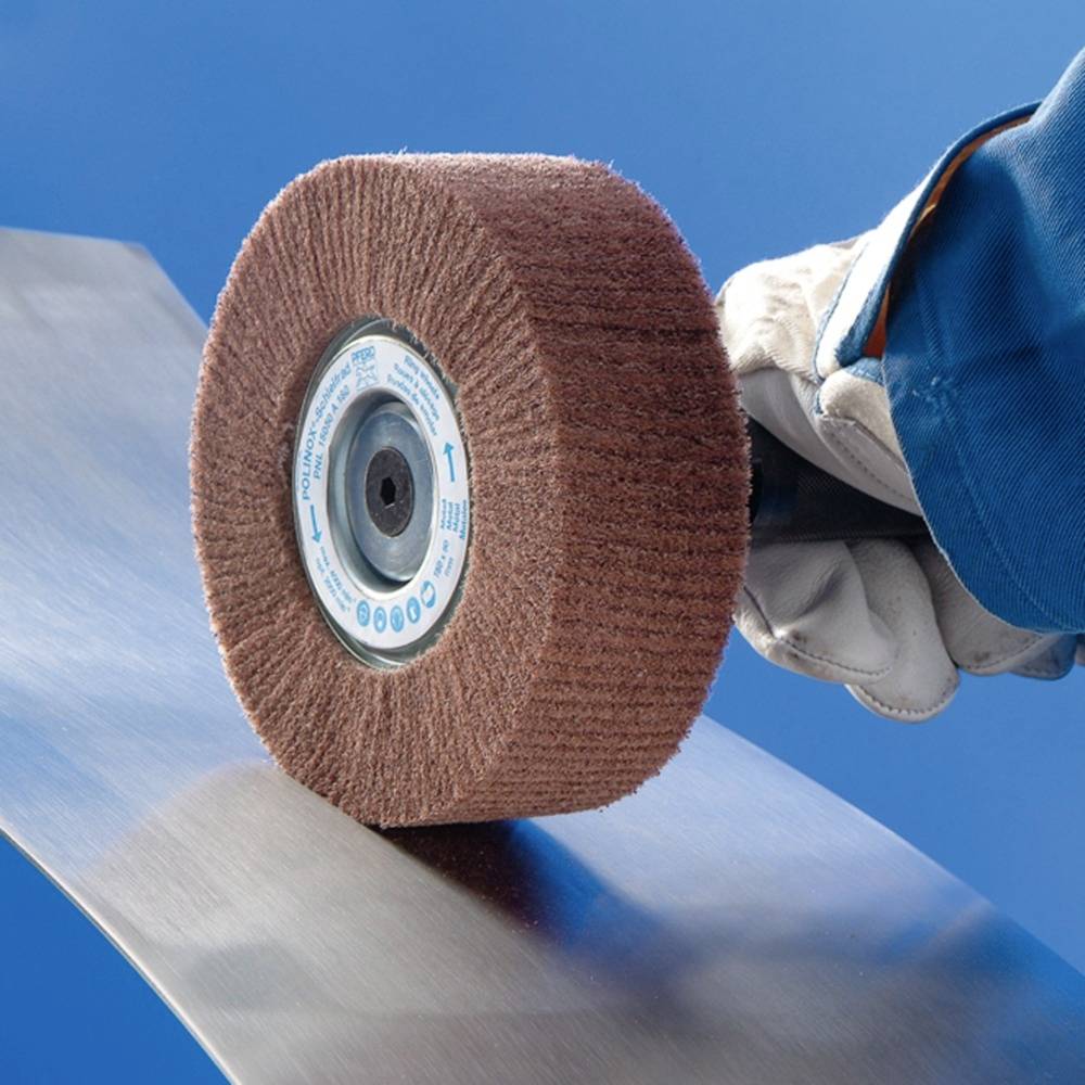 Une main gantée tient un disque de polissage en rotation sur une pièce métallique afin de lisser sa surface.
