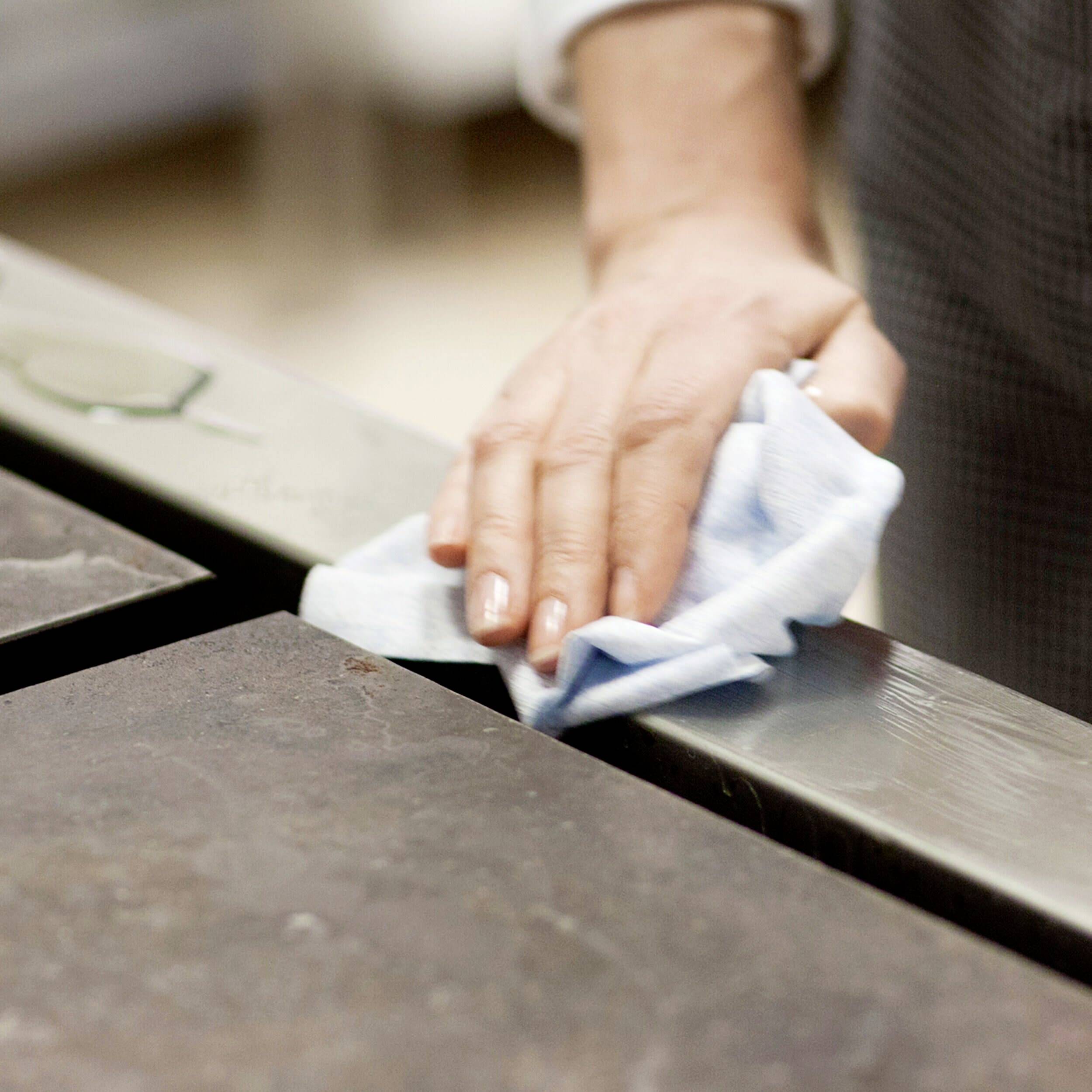 Une main essuie une surface de table sombre avec un chiffon bleu.