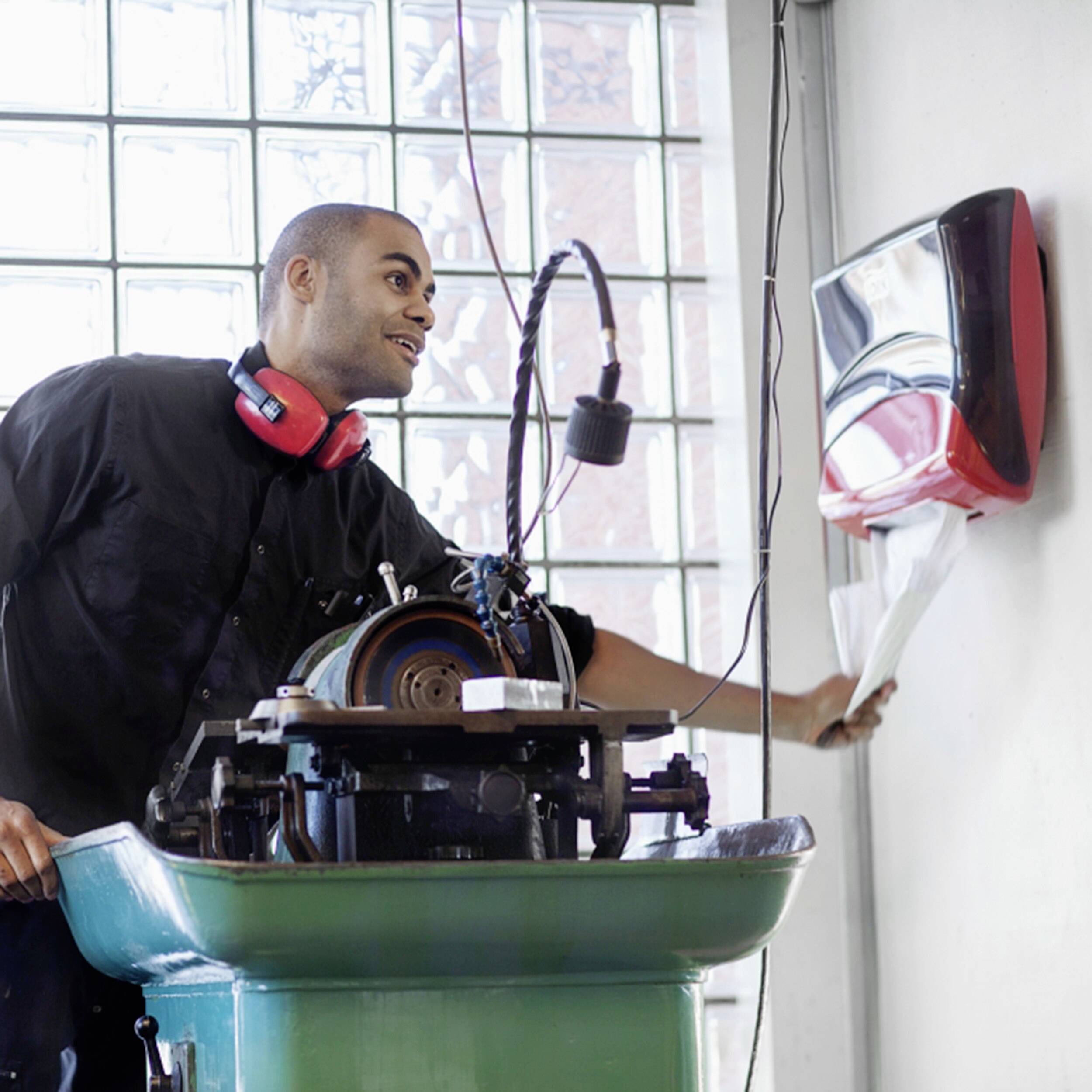 Un homme en tenue de travail utilise des essuie-mains en papier à côté d'une machine à coudre dans un atelier lumineux.