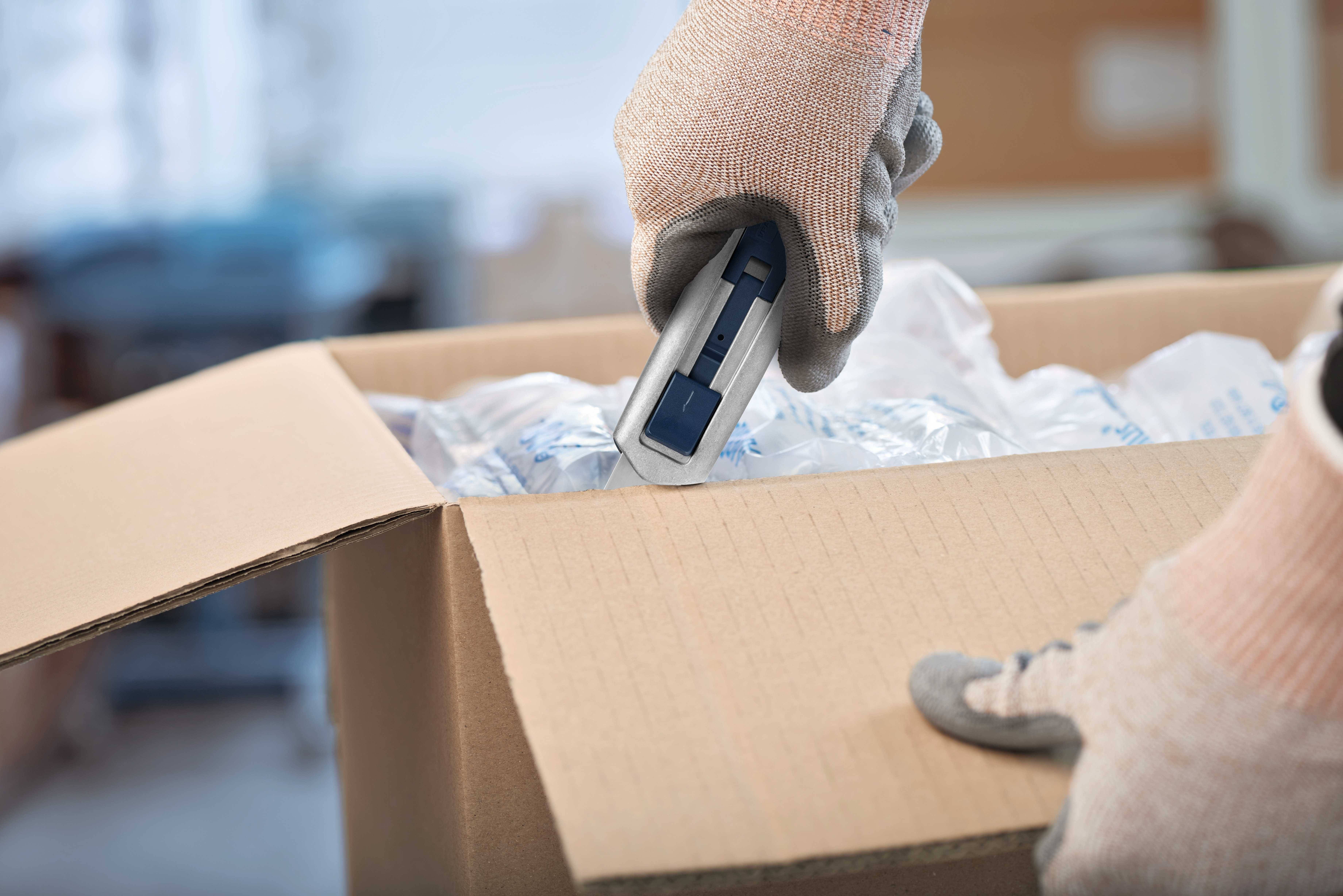 Une personne porte des gants et utilise un scanner manuel pour numériser un carton. À l'intérieur du carton se trouvent des emballages en plastique.