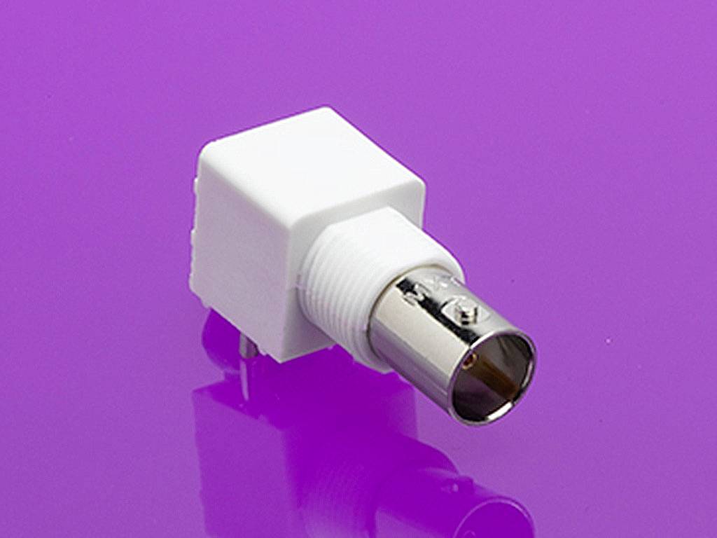 Un adaptateur blanc rectangulaire avec une connexion métallique sur un fond rose. L'adaptateur présente un design de connecteur BNC.