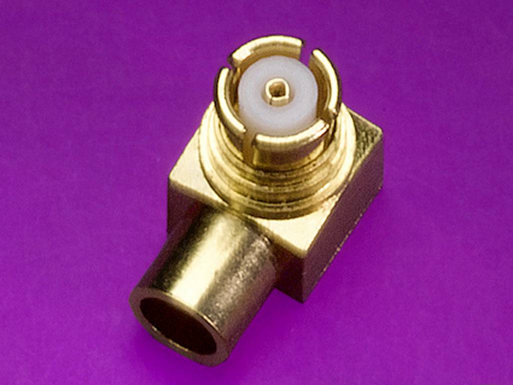 Un connecteur coaxial doré avec un socle rectangulaire sur un fond lilas, illustrant une technologie de connexion précise.