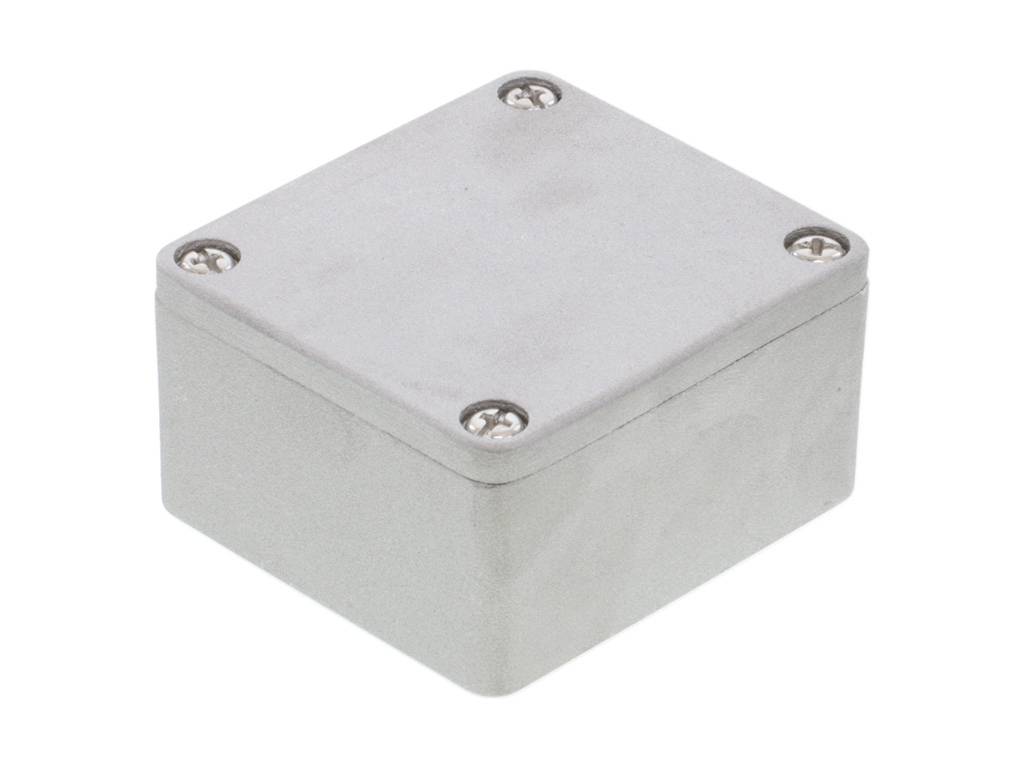 Petit boîtier métallique gris, carré, avec des fermetures à vis dans les coins.