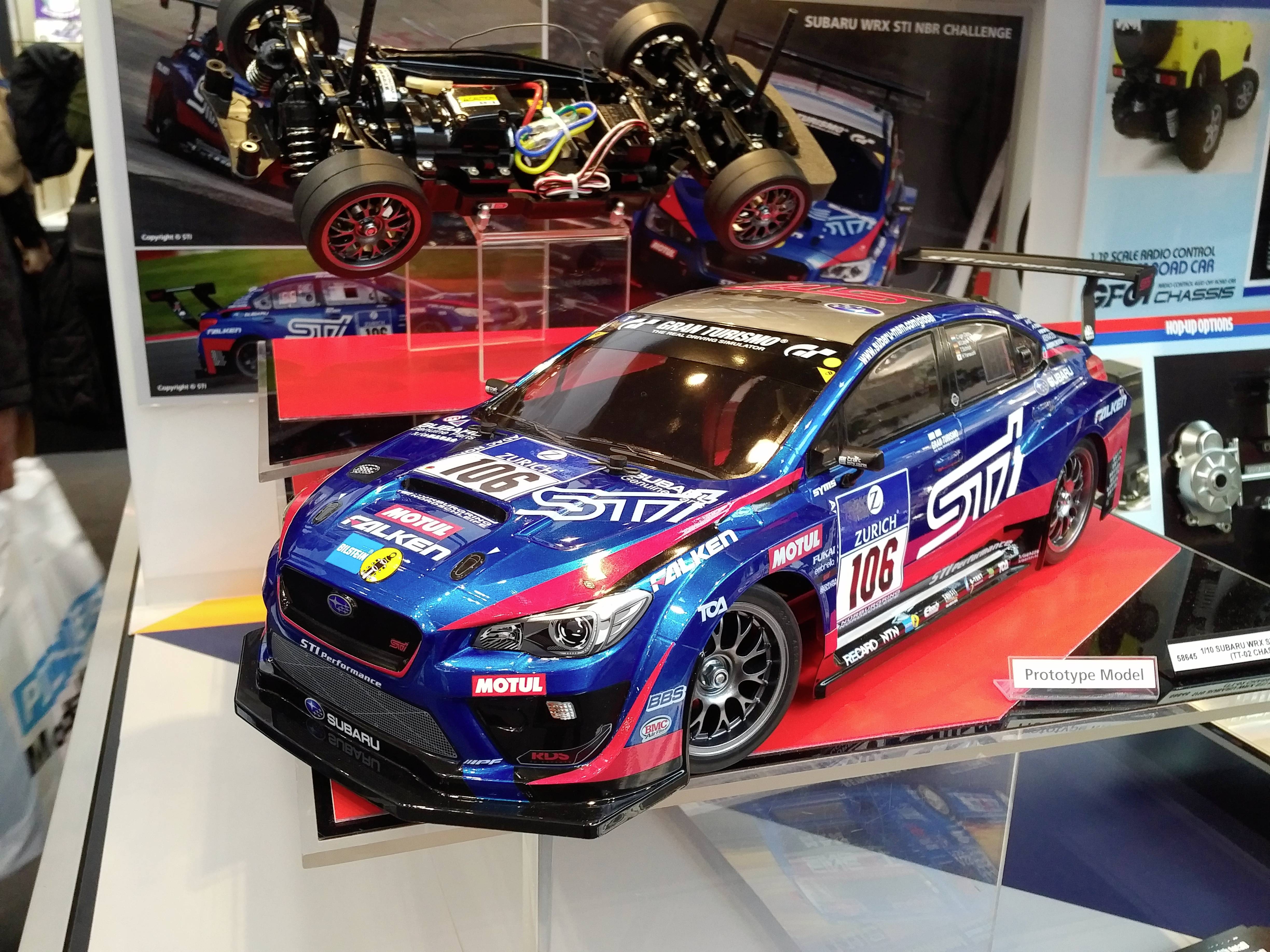 Une miniature détaillée d'une Subaru WRX préparée pour la course est exposée sur un socle, entourée d'autres détails techniques et de photographies.