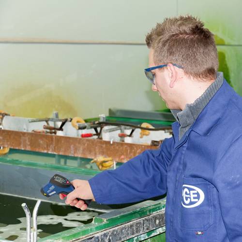 Un homme portant une blouse bleue mesure la température d'un liquide dans un bain industriel à l'aide d'un thermomètre.