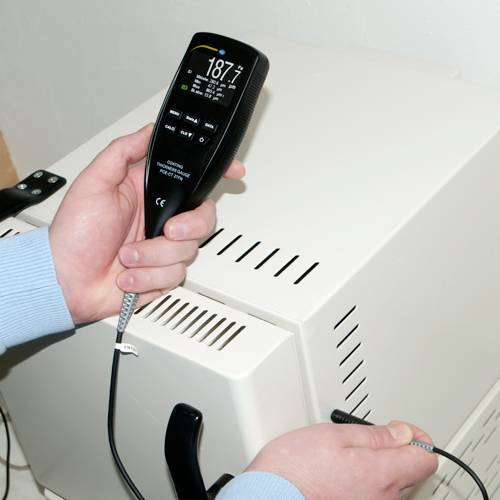 Une personne tient un appareil de mesure de température à côté d'un radiateur. L'écran affiche 18,7 degrés et d'autres données de mesure.